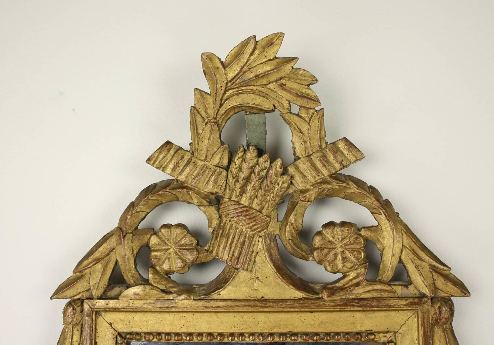 A beautiful mid 18th Century carved and gilded French wall mirror with decorative detail in the shape of a wheat sheaf and classical floral garland. The glass with some spotting a crazing, adds marvelous visual interest. There are some small chips