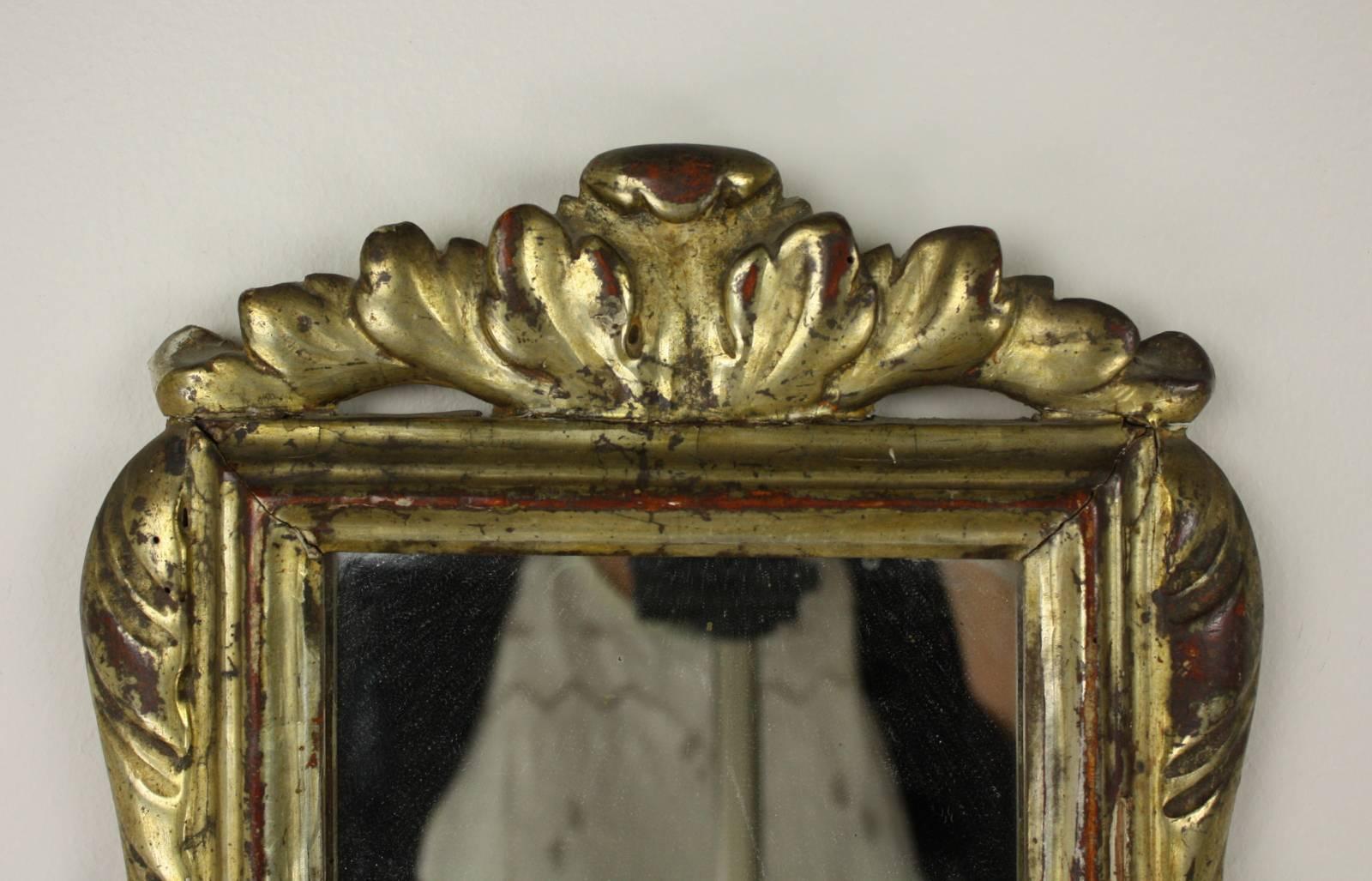 A turn of the 19th Century Baroque gilded mirror from Italy with stylized lush leave details and very good red show-through.  Some wear on the mirror adds to the look.  The smaller size makes this piece perfect for the powder room or a small