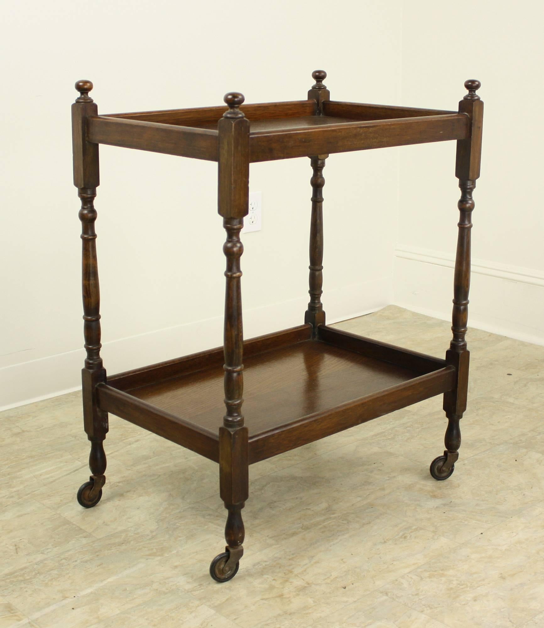 Elegant two-tier bar cart. Rich oak, with decorative barley twist legs and charming finials. Original castors. There are 19" between the shelves. This cart would make an interesting end table.