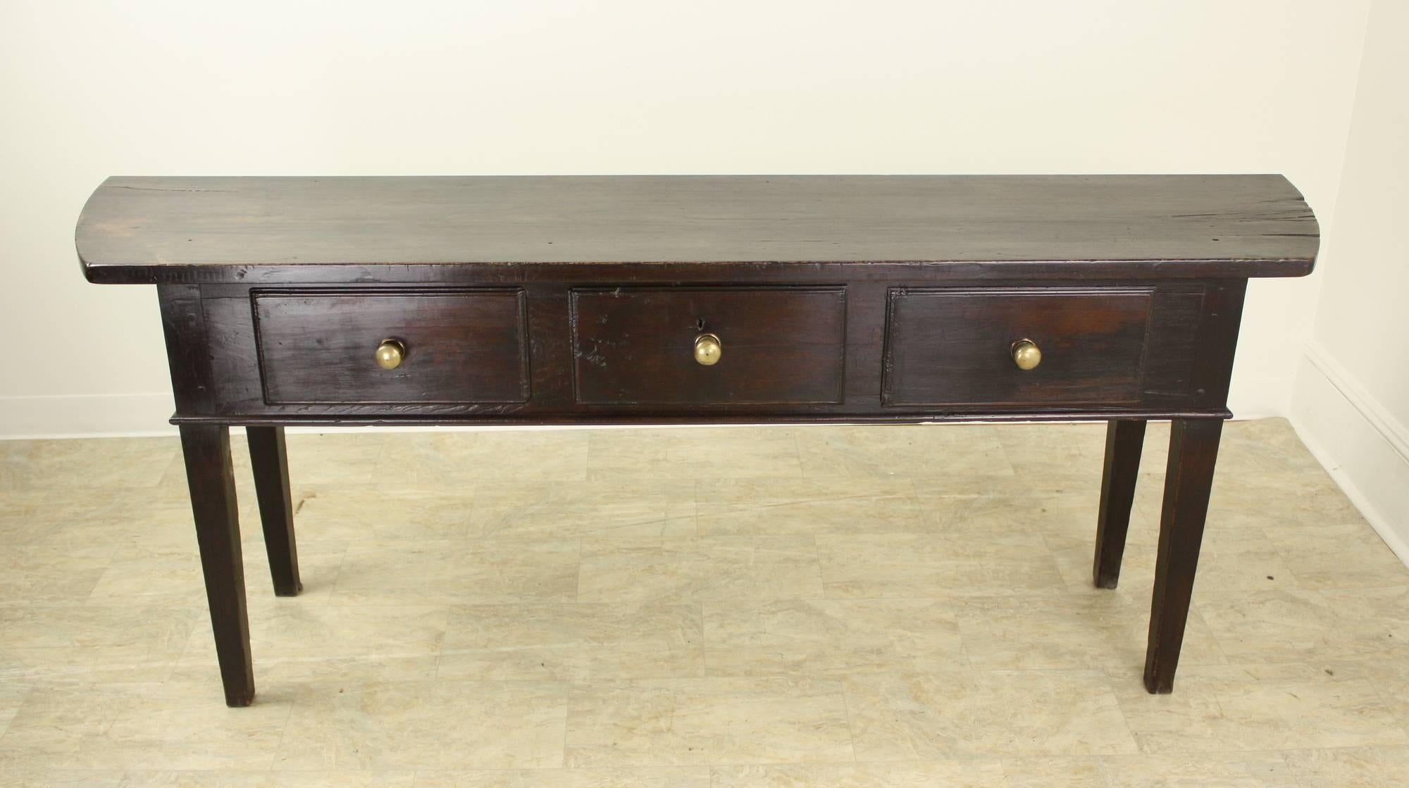 This long and elegant console table, in dark, rich fruitwood, is dramatic and impressive. The ends on each side of the top are shaped much like a D-end table, which is quite unusual and eye-catching. The top's fruitwood grain is most attractive