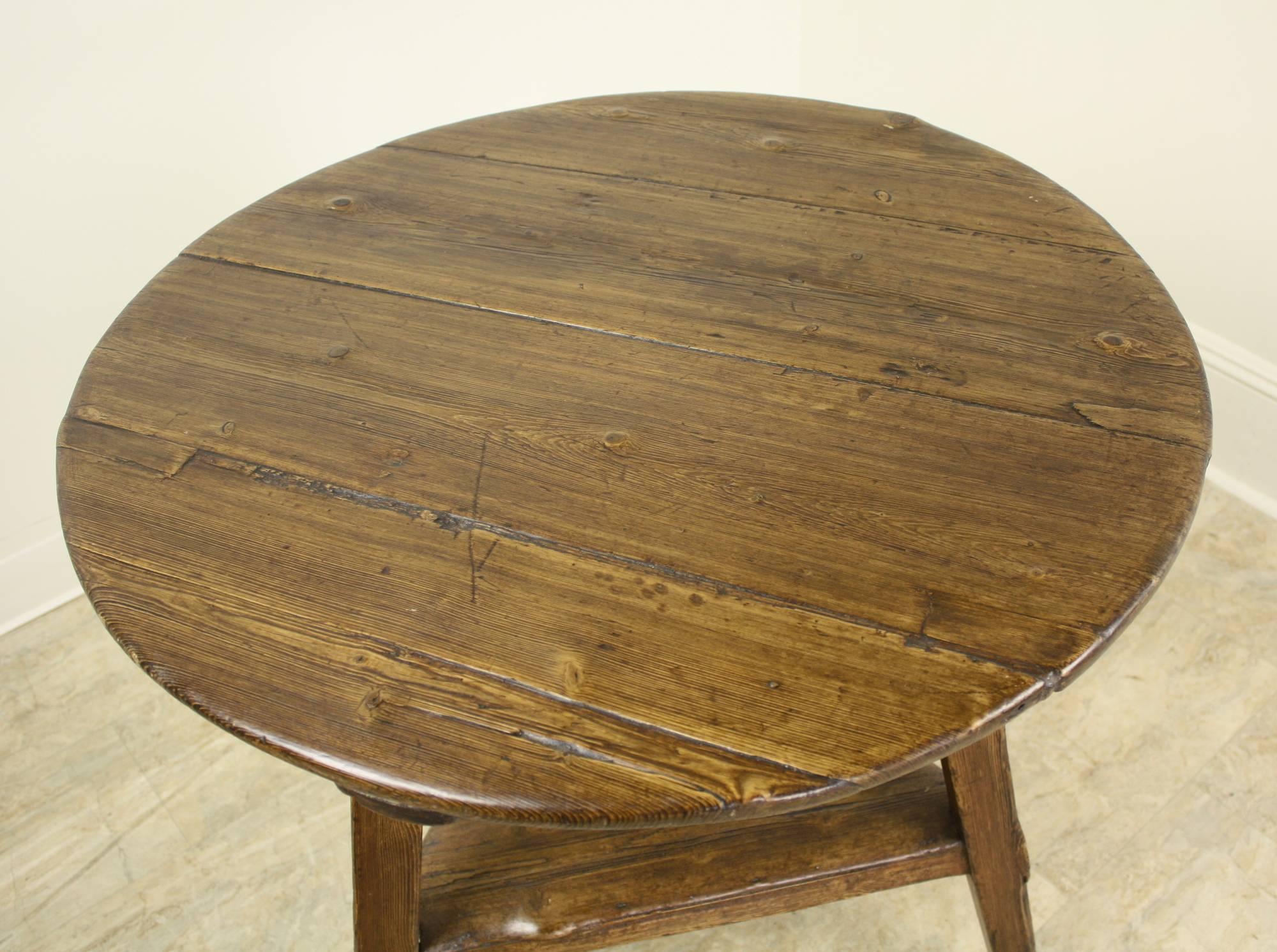 A pine cricket table with exceptional dark rich color, glow and patina.  The use of full grained wood, complete with natural knotholes and textures makes this a fine example of handmade country antique furniture.  Typical three-legged table, with