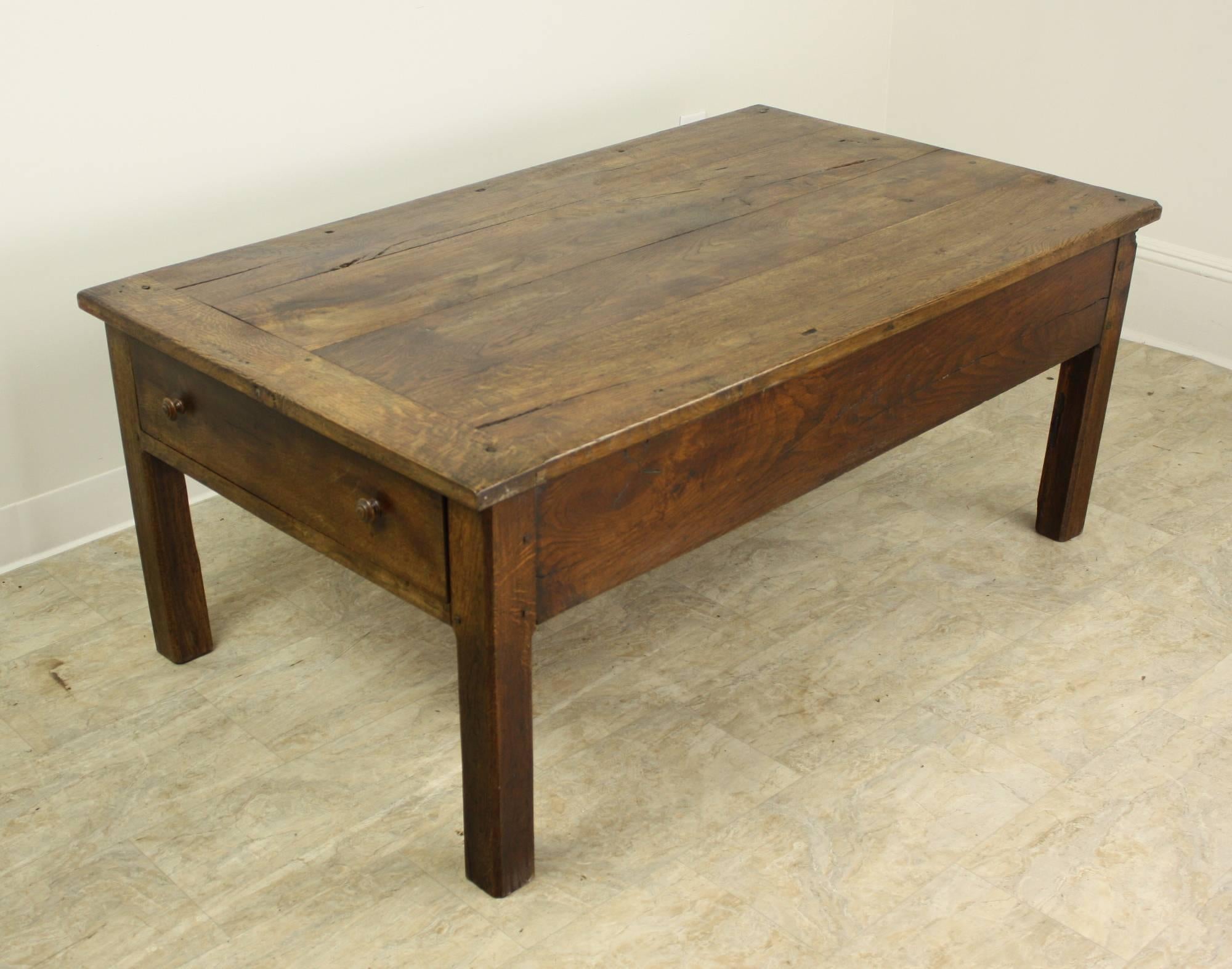 A handsome silhouette in well patinated early oak. This coffee table boasts two  drawers, one on each end, nice grain and a rich warm color. The top has some areas of light distress, which lends the piece good character. The strong legs add another