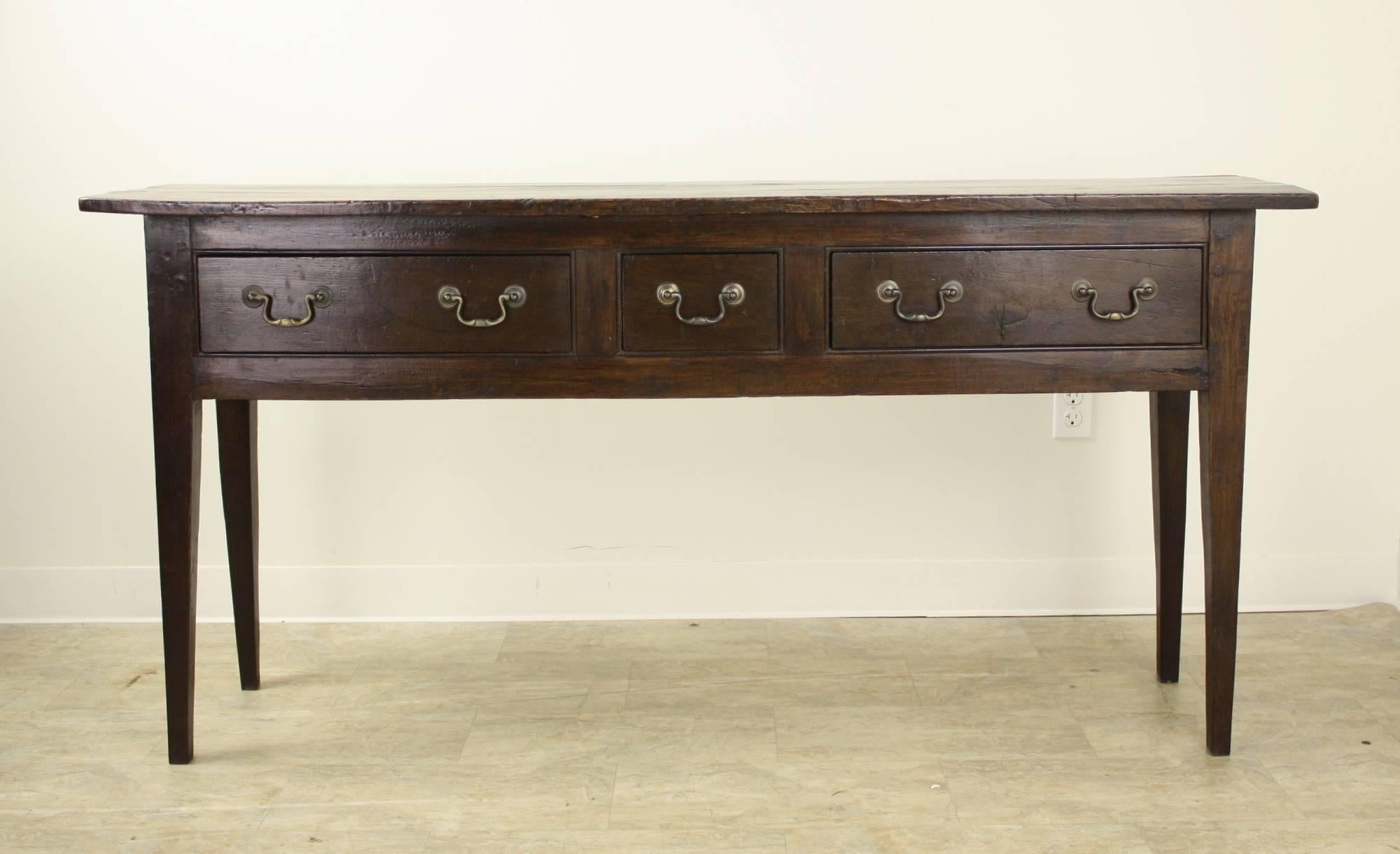 This richly colored dark chestnut piece is a very impressive long console table. Three drawers include a charming small center drawer. Legs are classic long and tapered country style, with sturdy pegs. Tho longer, the depth of this server is narrow,