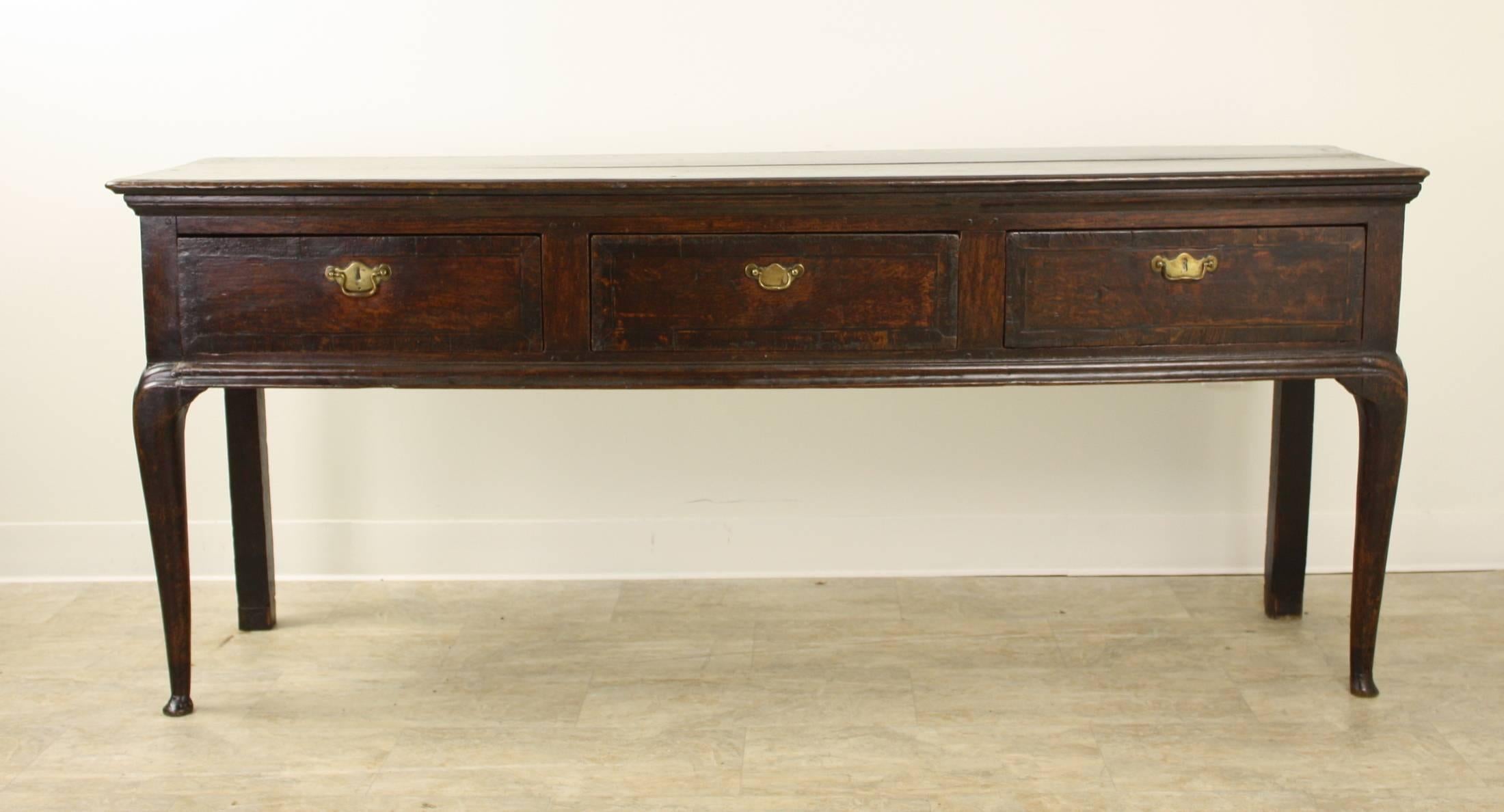This dark oak server is an outstanding look. Wonderful moldings above and below the apron, and all around the top. There are three drawers, each with an original brass handle of the period. The front legs are shaped, and have little pad feet,