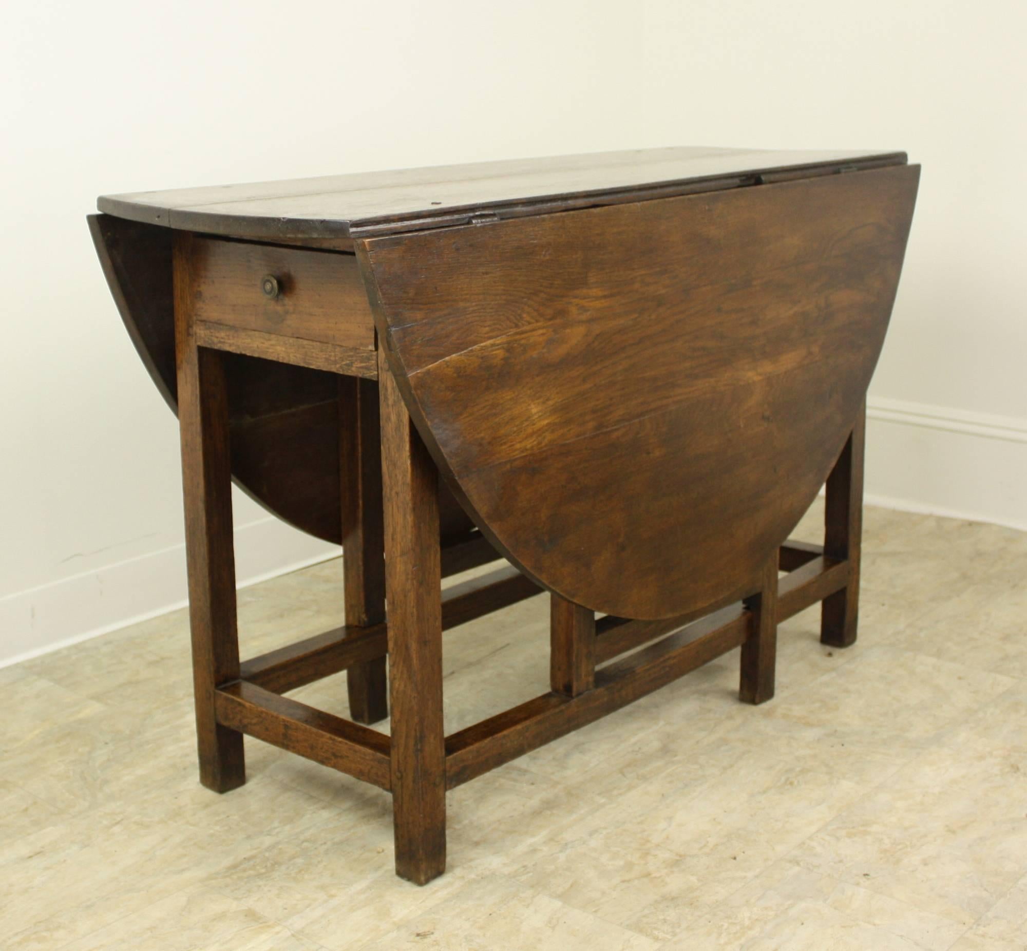 Just shy of five by four feet, the top is a good size dining or breakfast table. This is an example of a very early gateleg, with well proportioned drop leaves. The color is a nice warm oak. There is a drawer on one end, and seating all around is