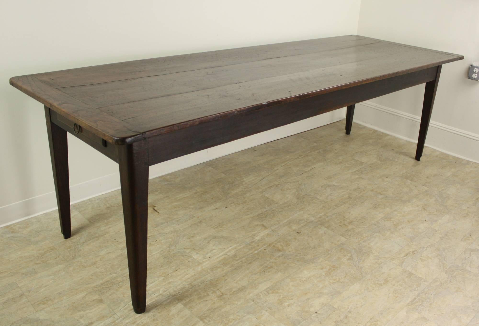 This long table is also wide, providing excellent space for dining. It is very good looking, and provides lovely attributes. There are bread board ends, with slightly rounded ends on the top. Strong tapered legs, a rich color and patina and a drawer