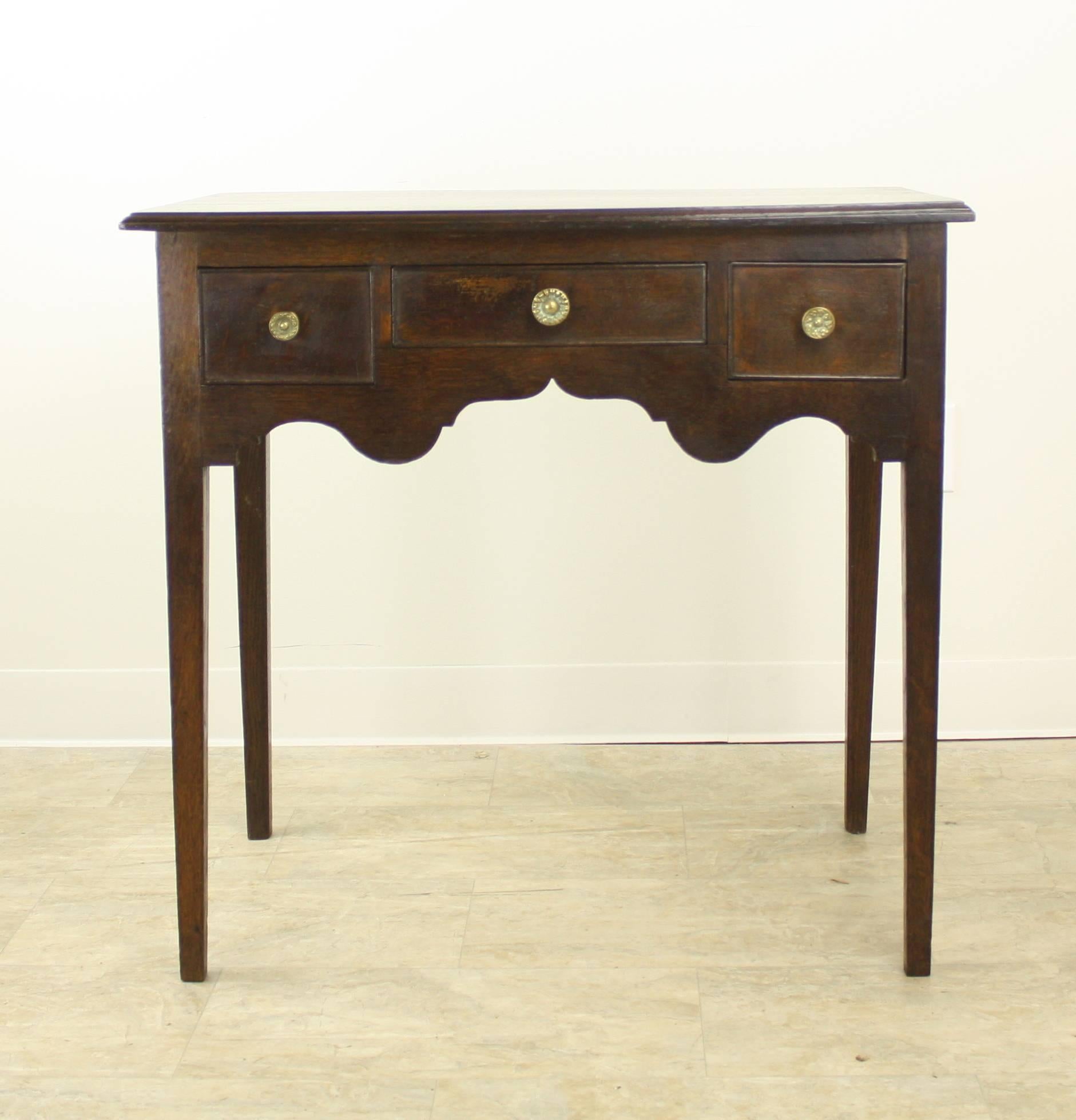 A stunning Classic period lowboy, a side table with lovely scalloped aprons, having three front drawers. The top has a very handsome molding around the edge, and the base is comprised of elegantly tapered slender legs. Color and patina are rich dark