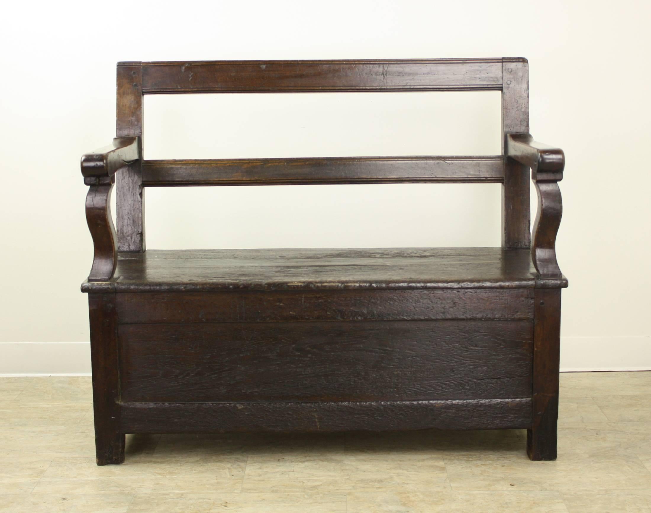 A very nice, rustic, sturdy bench, often found near the fireside, to hold wood or kindling. In this case, the storage area is a pull-out drawer on one side. Terrific deep color and patina. Really nicely shaped arms.