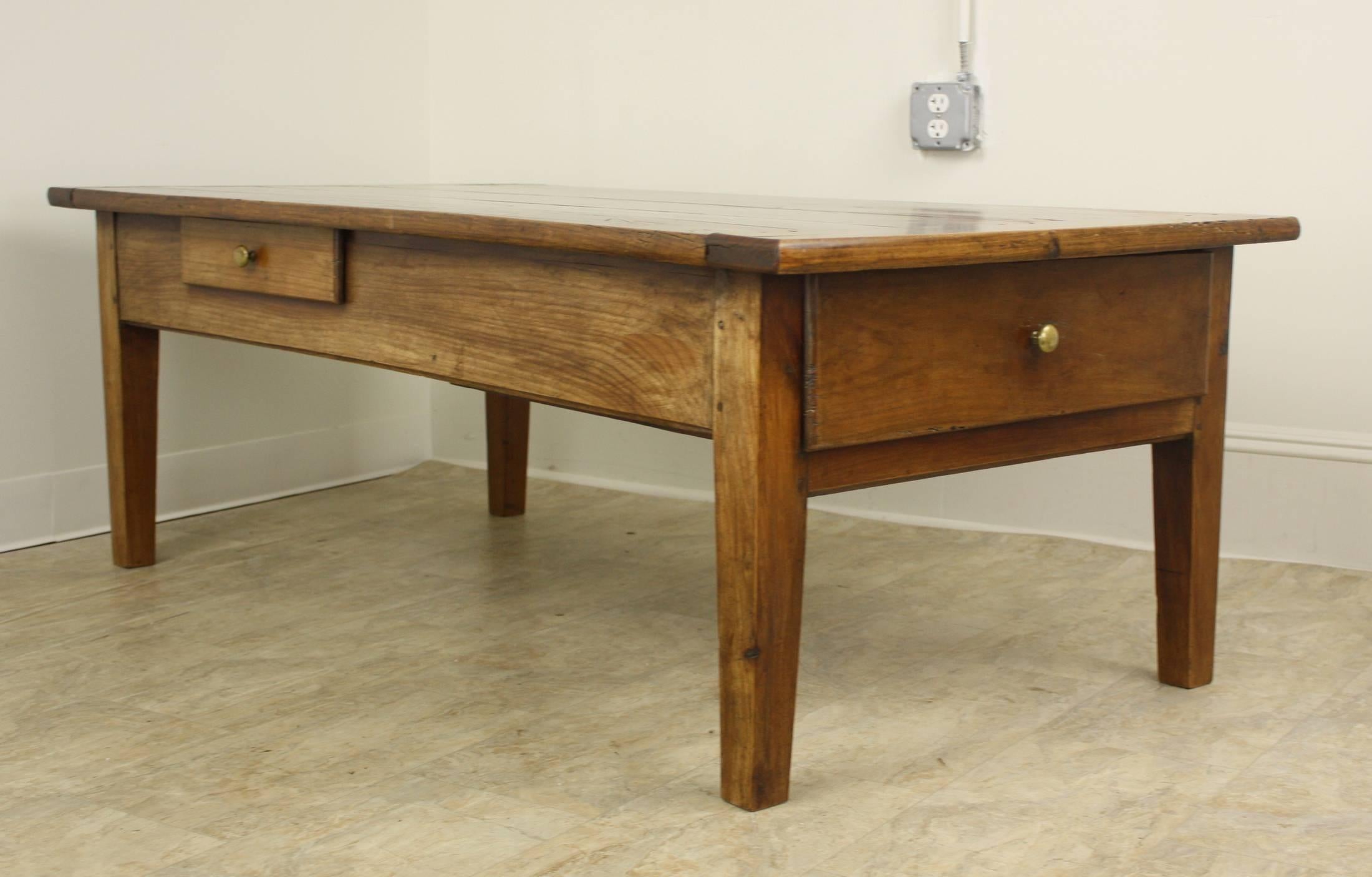 A very lovely warm rich honey cherrywood in a large size, very attractive coffee table. There is a large drawer on one end and a smaller drawer on one long side. There is a breadboard end, and the legs are chunky and sturdy yet have a nice Classic
