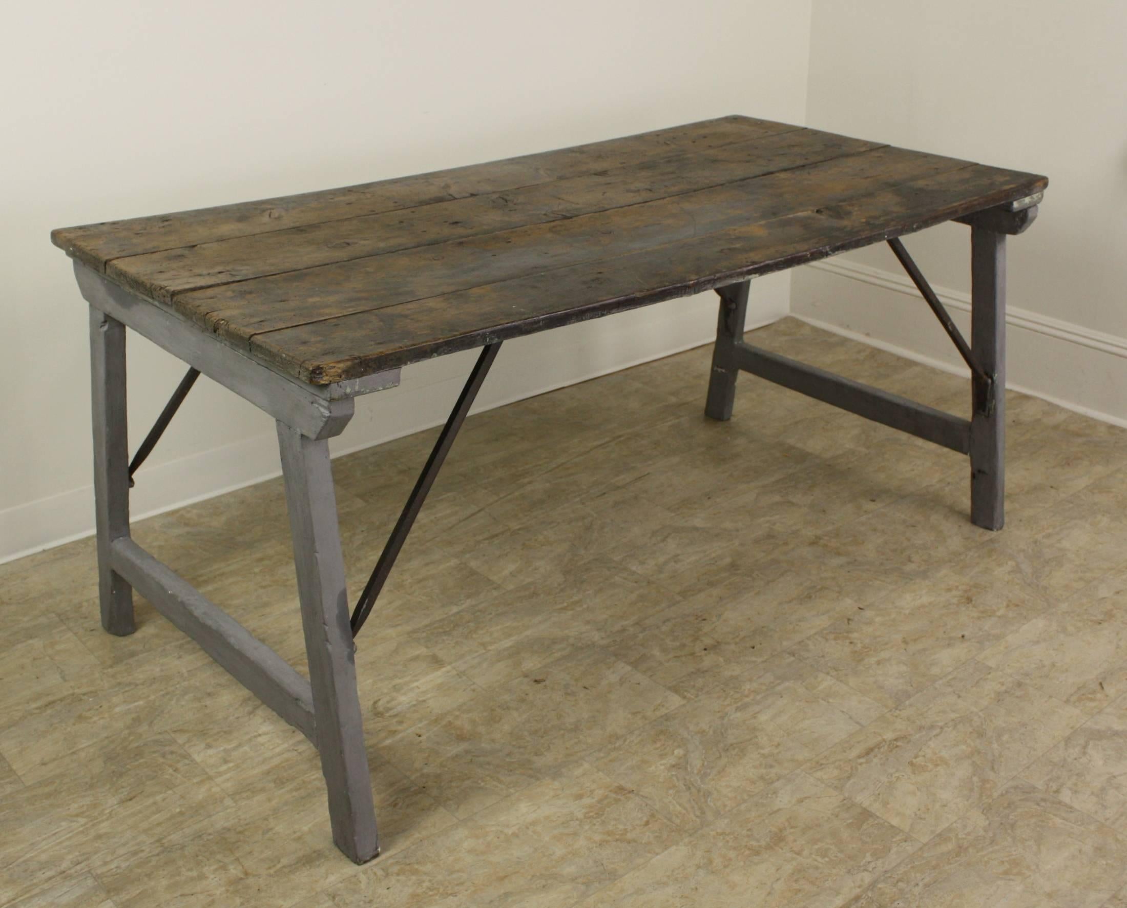 A folding country table with fabulous distress on old paint, giving it a lavish and dramatic look. The top is fashioned from four rustic planks, and the metal supports fold into the table with a turn of the screws.