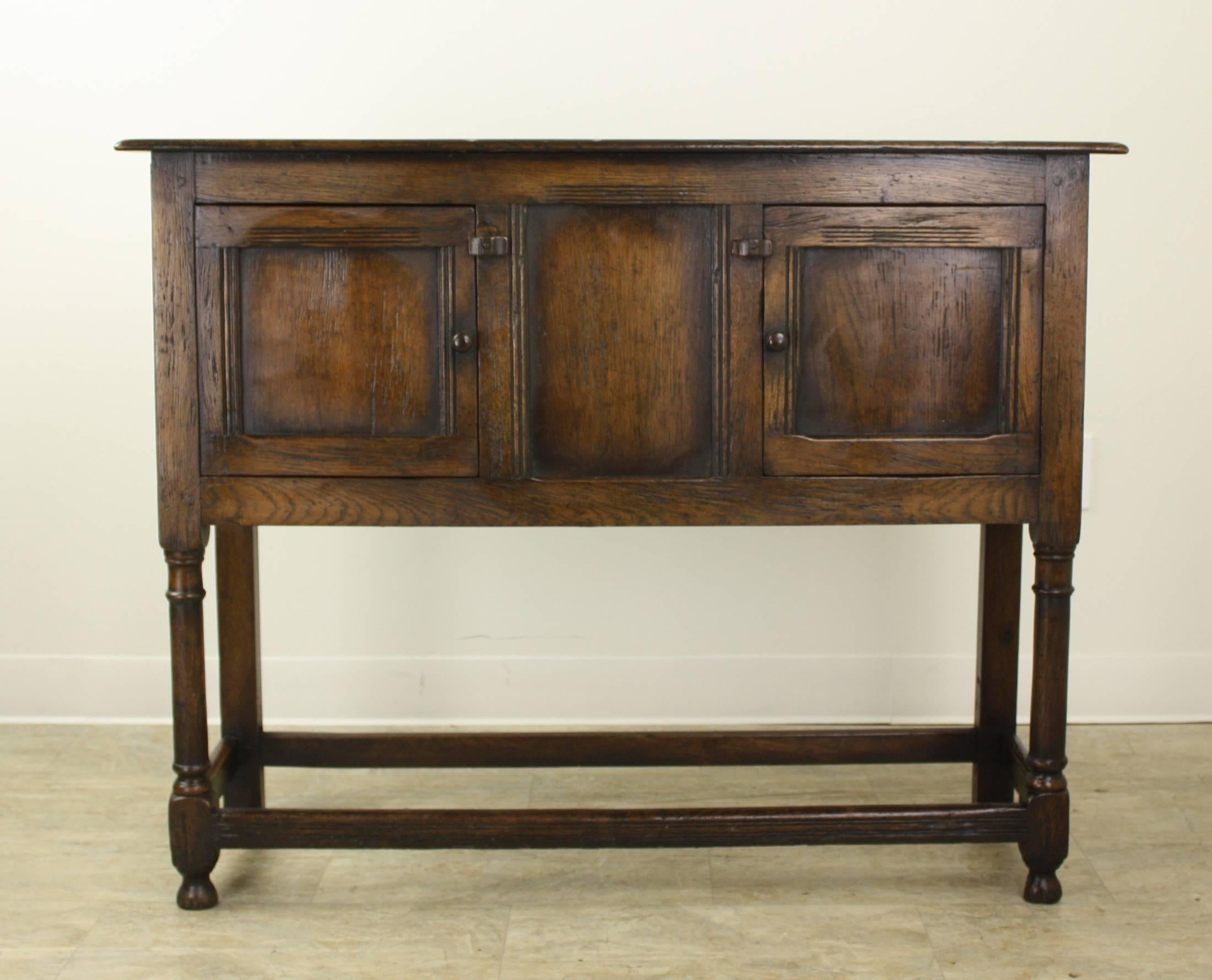 A charming English oak server with a stretcher base, simple latch closures, and inset panels on the doors and sides. Rich color and lovely patina complete the look. Very sturdy. The doors open and shut easily and the top is in very good condition