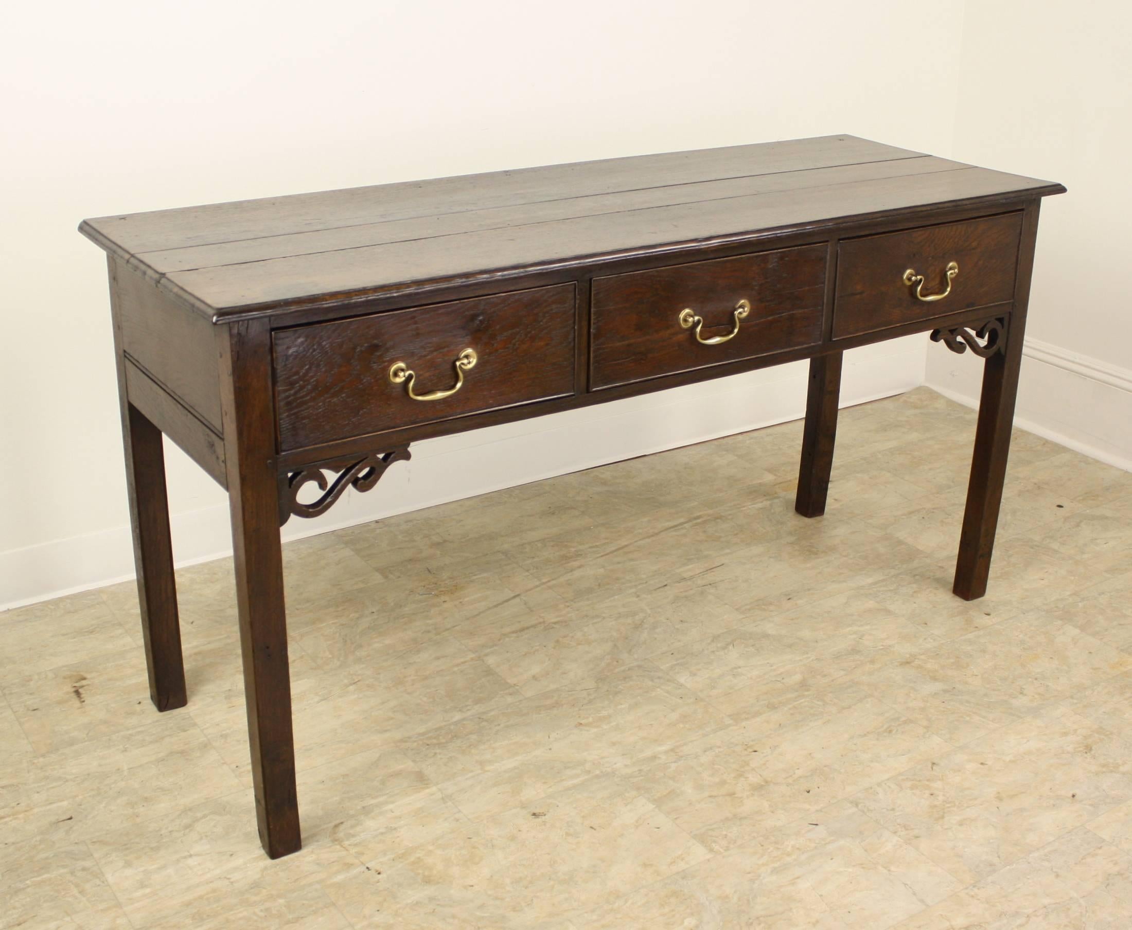 A glorious smaller server, with fine patinated oak grain and delightful fretted details at the corners. Three generous drawers, period appropriate square legs and solid brass hardware complete the look.