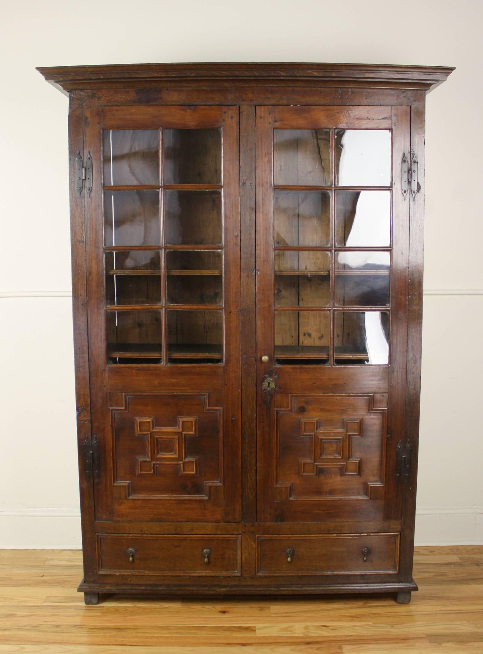A splendid dark bookcase in fruitwood and oak, with original leaded glass panes. Handsome mouldings at top and bottom. The geometric pattern on the doors is quite modernistic despite the age of the piece, lending it a timeless quality. Five shelves