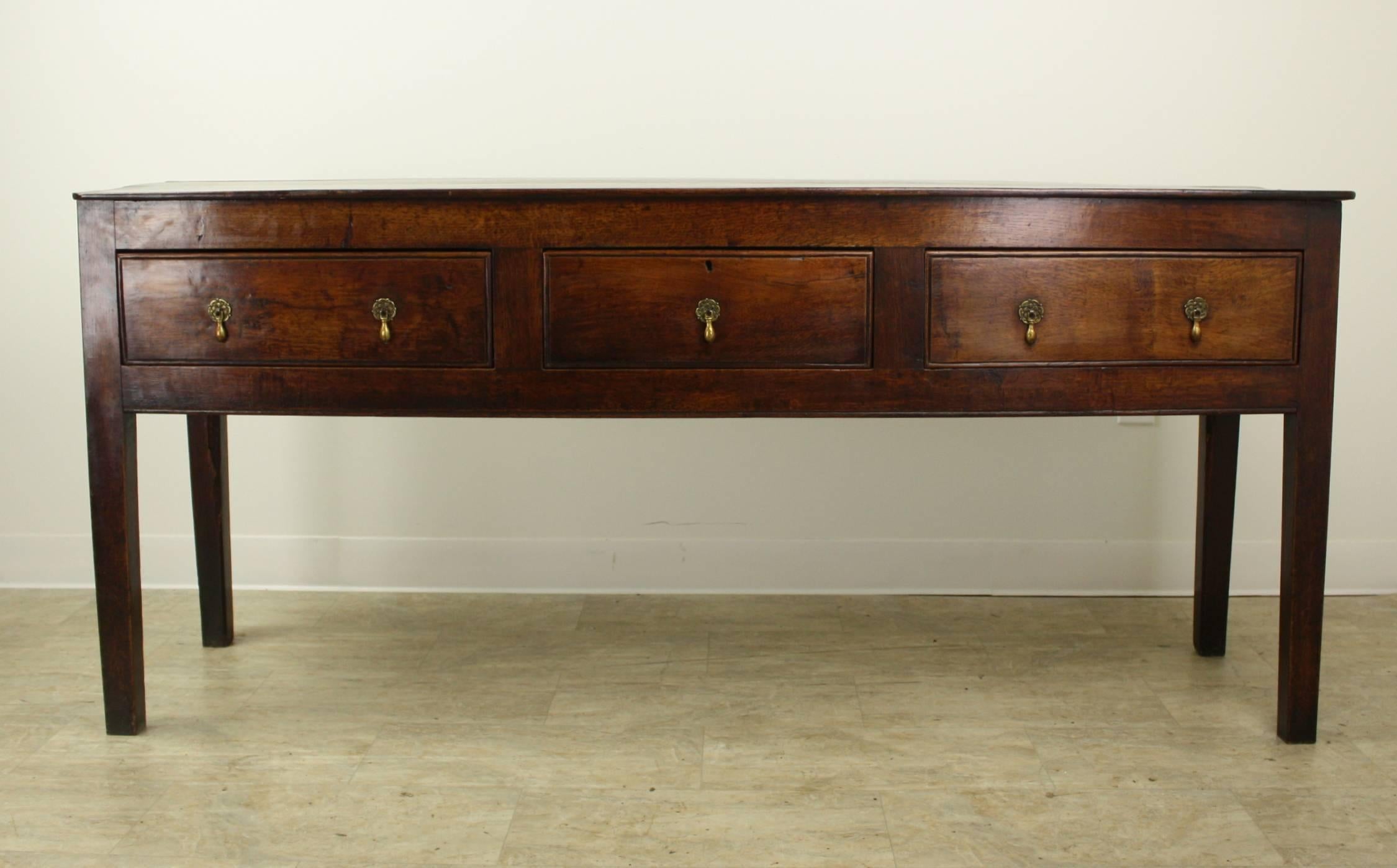 An early Welsh oak three-drawer console with a simple elegant Silhouette. The oak has a beautiful grain and color. The straight legs and brass teardrop handles complete the look of this sideboard. Would make an arresting hall table or sofa table.