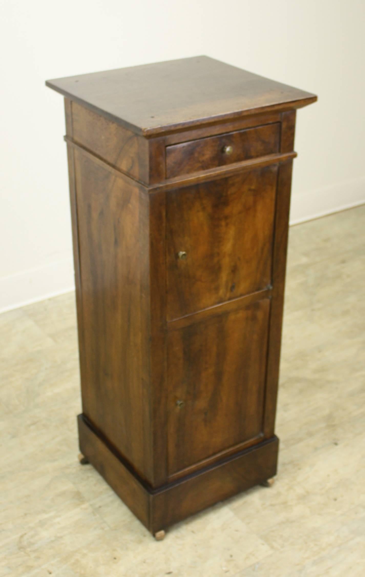 Small attractive cabinet with remarkable walnut grain. One sweet drawer over two cupboards. Decorative moulding and base completed by original wooden castors. Would work as a small lamp table.