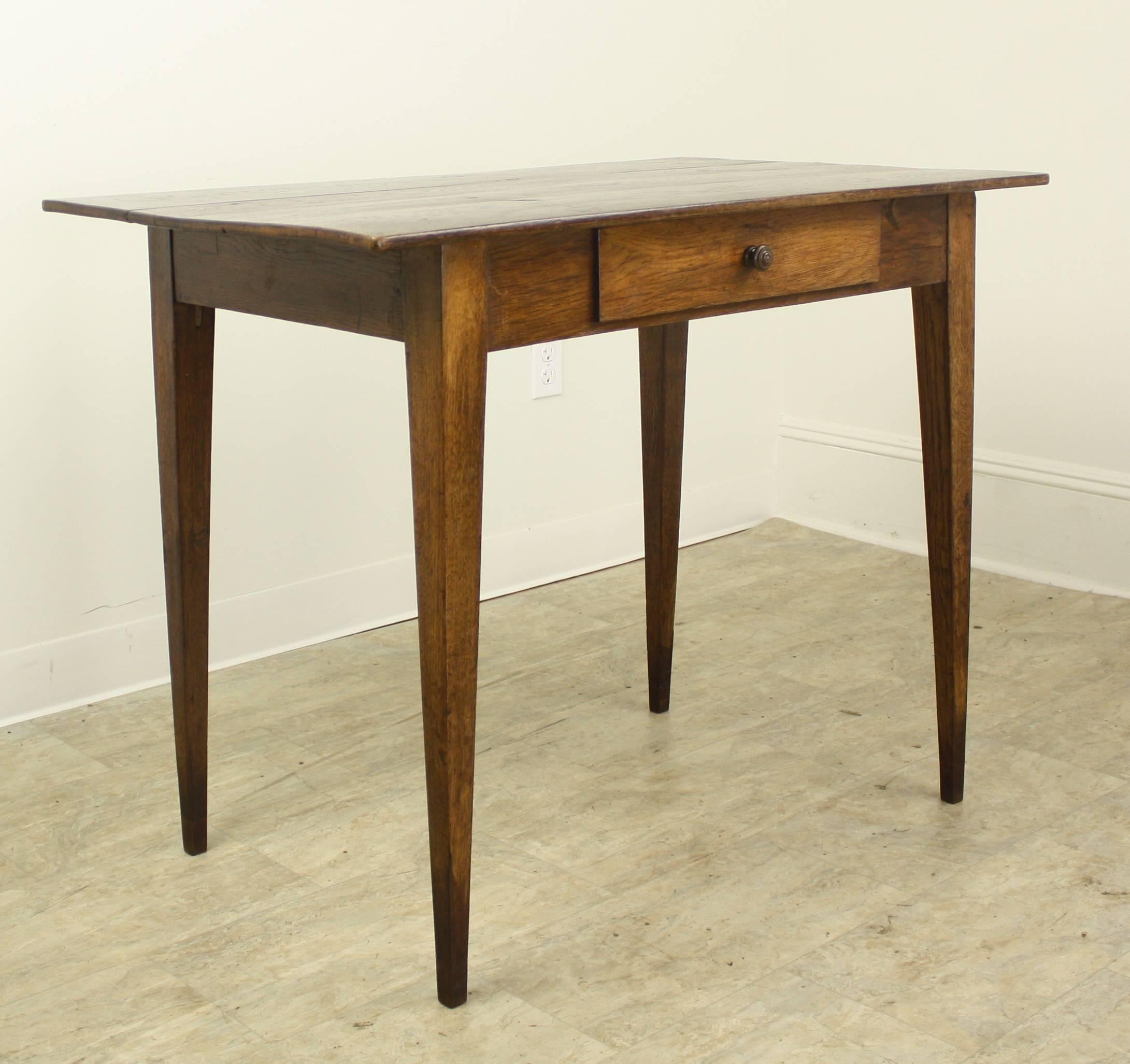 A graceful antique oak side table, with a single drawer on slim tapered legs. Wonderful grain, color and patina. There is a little warp to the legs which renders the piece slightly asymmetrical, but still completely stabile. No wobbling! Apron