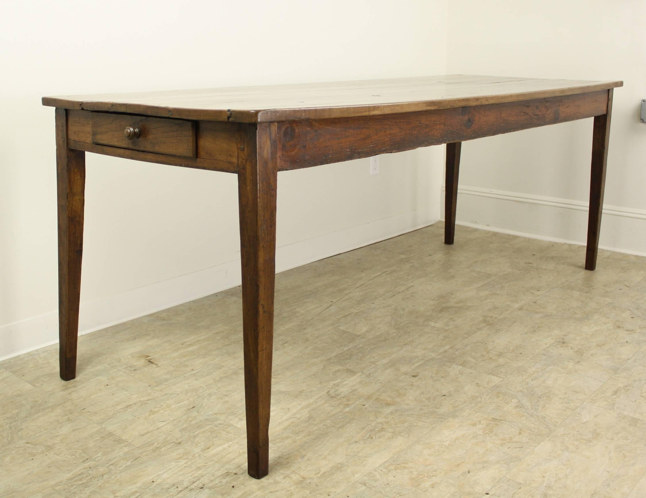 A splendid cherry farm table with warm color and gorgeous patina. The table top has several wonderful knotholes and naturalistic features, which gives the piece great character. Elegant tapered legs and a single drawer at the end complete the look.
