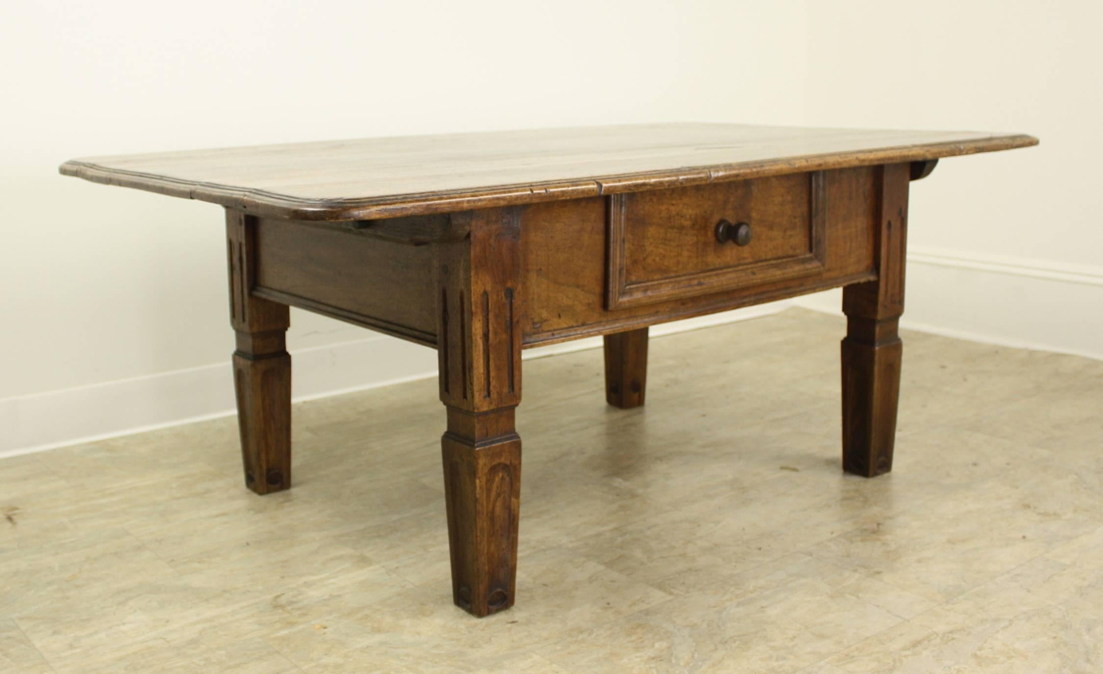 A beautifully grained Alsacian walnut coffee table. The top has wonderful color and patina with extravagant grain, while the look of the front is punctuated by a single carved drawer. Chunky stylized legs complete the look.
