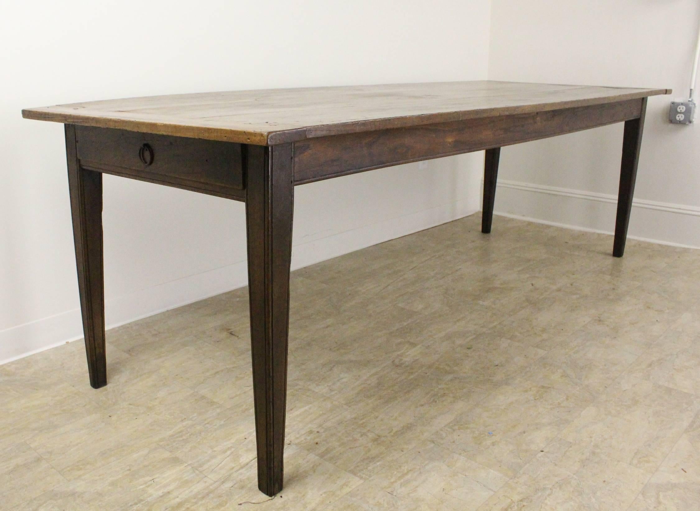 A large antique elm farm table with handsome proportions and lovely color, grain and patina. The elegant tapered legs and single drawer at the end add a nice design note. It should be mentioned that the apron is 25 inches high on the long sides and