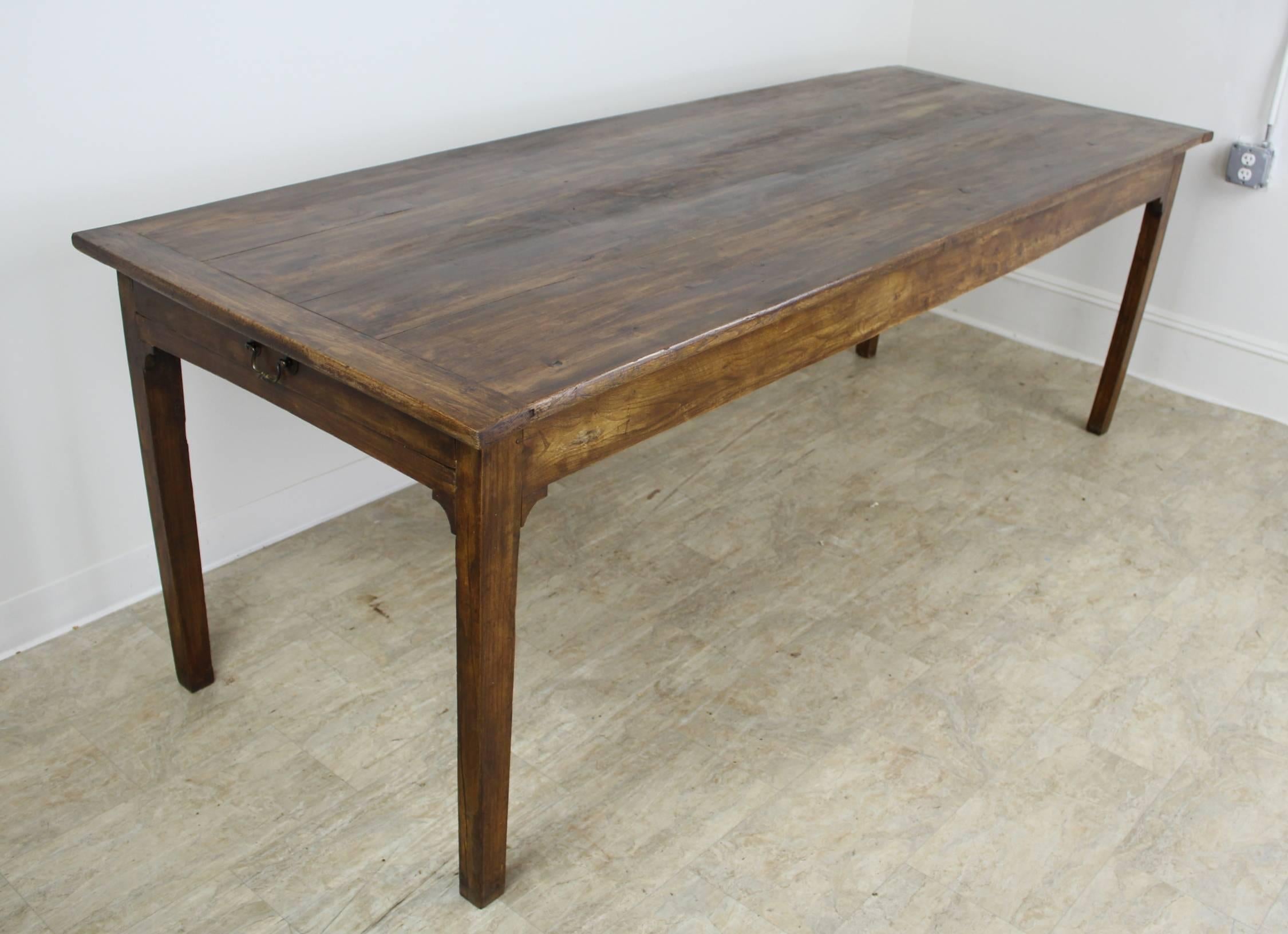 A wonderful elm farm table generously proportioned for maximum seating with 81 inches between the legs on the long side. A drawer at either end or bread boards on top add interest, as do the carved supports under each leg. The grain, color and
