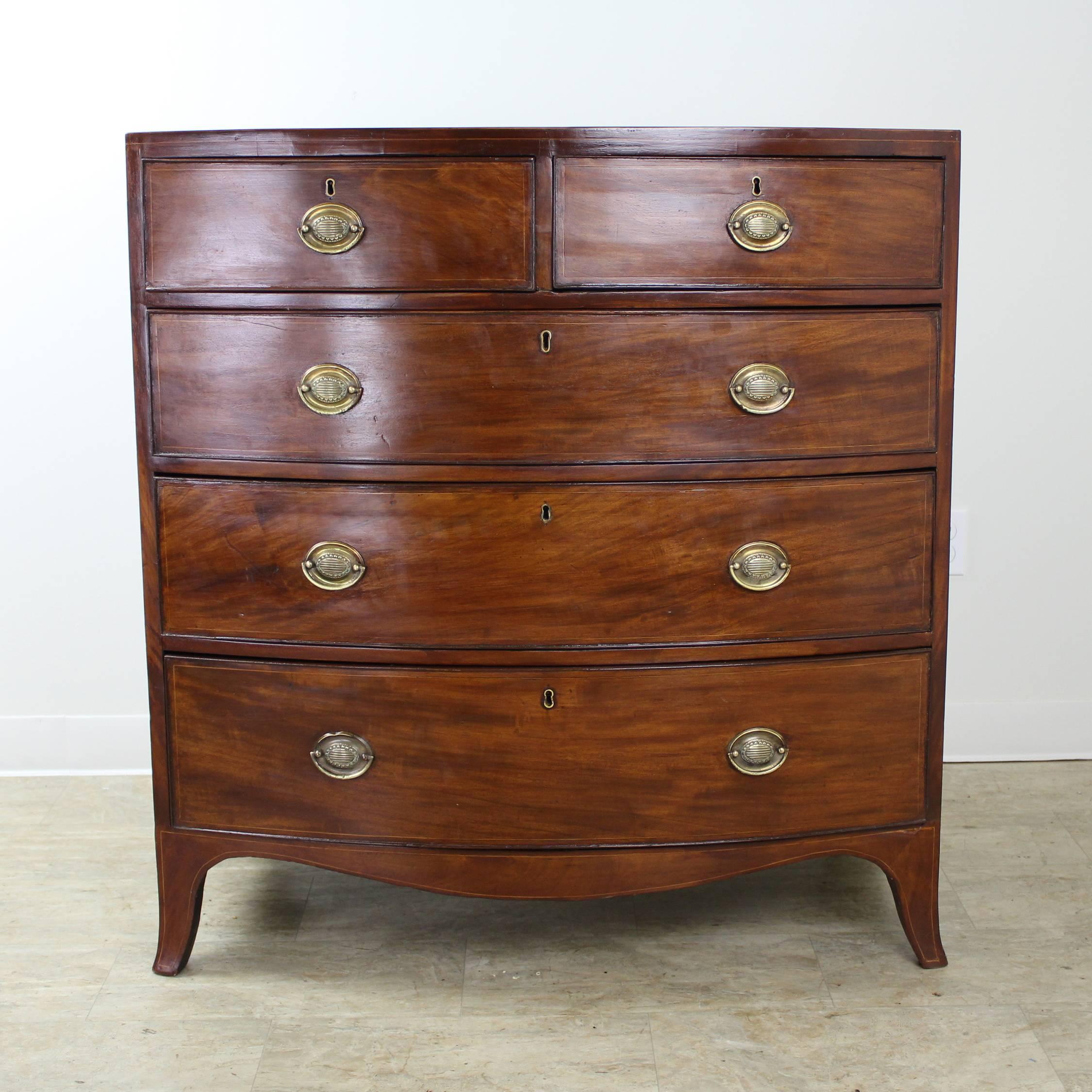 An elegant antique bowfront bureau. The mahogany is a rich medium color with a lovely grain. Details of note include the delicate satinwood stringing, cockbeading on the drawers, and beautifully wrought brass drawer pulls. The graceful French style