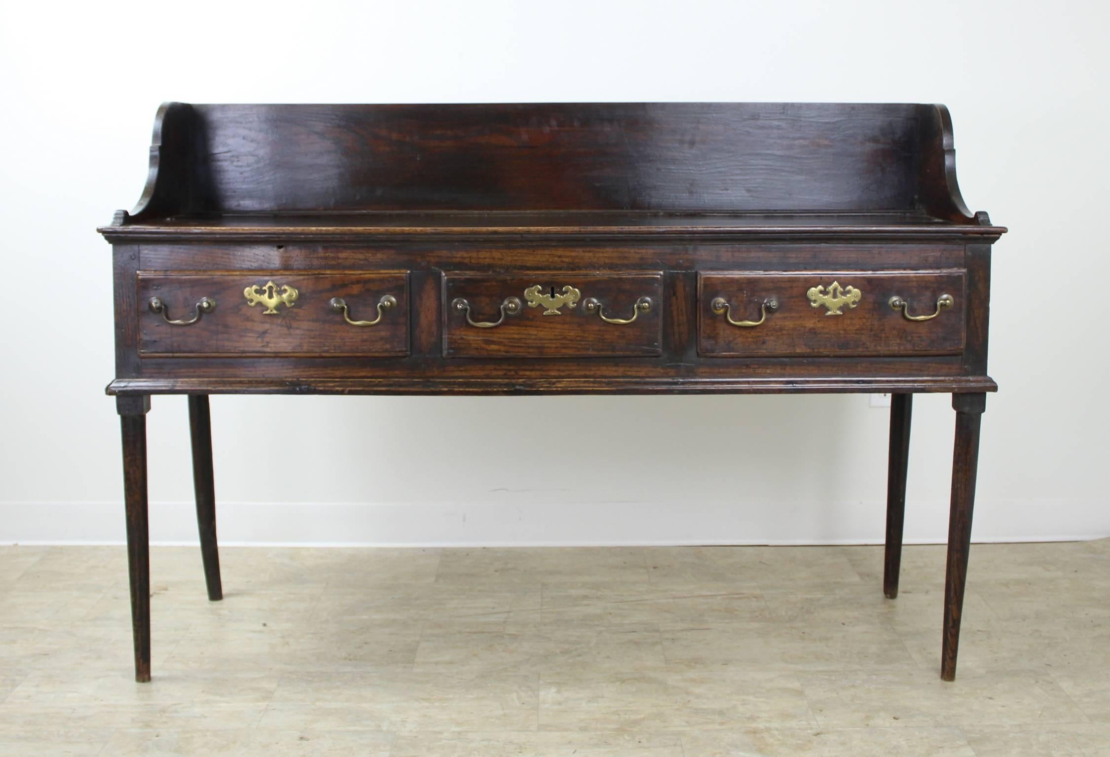 An early English period oak server with lovely grain and gorgeous wear and patina. The galleried back has a plate stop for display and the entire piece is trimmed with decorative mouldings. Three roomy drawers provide excellent storage. One of the