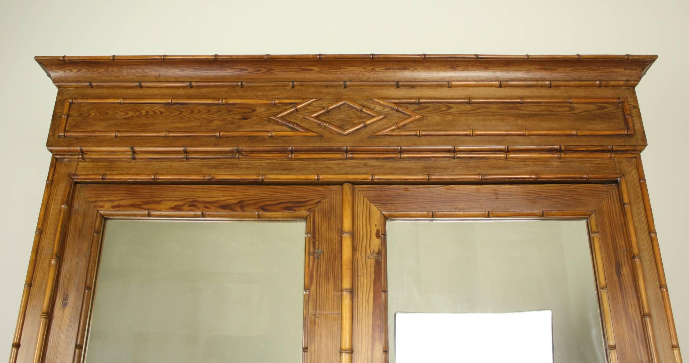 A large and imposing honey colored faux bamboo linen press or armoire from England. The piece boasts four roomy shelves, with two wide bottom drawers and three small interior drawers. The cornice and lower drawers feature beautifully fashioned wood