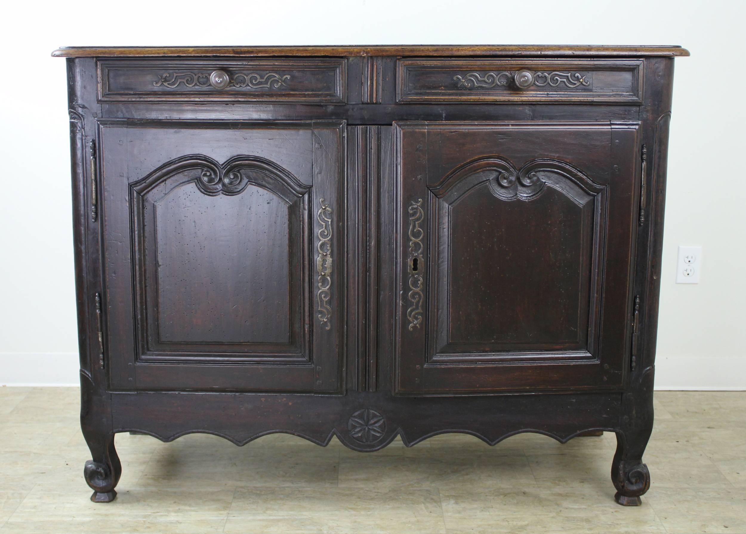 An early dark walnut buffet with fabulous iron hardware, snail feet, and a charming carved apron with a hand-wrought medallion detail. Inset panels on both doors and the sides. The wood has a rich, authentic patina and the single interior shelf is