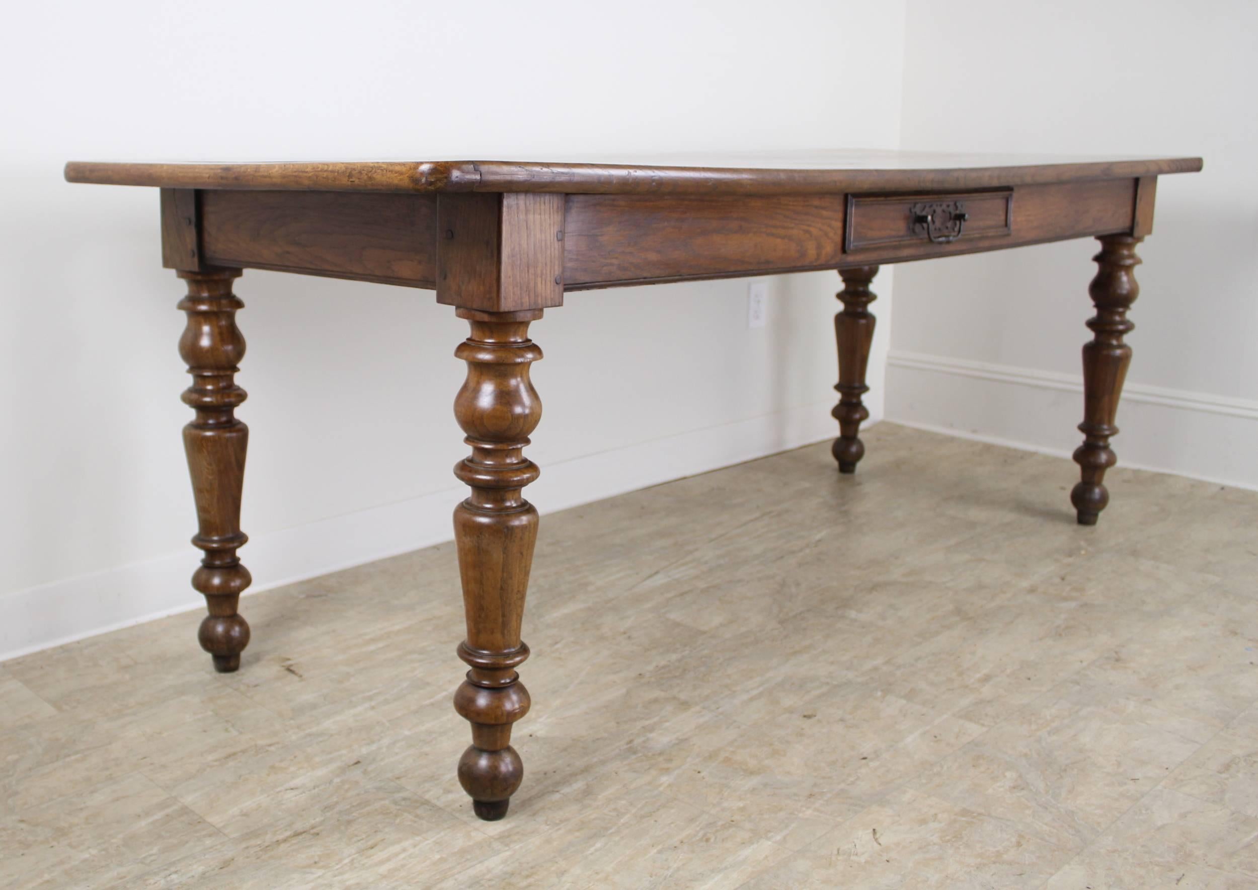 A chunky handsome oak farm table with thick turned legs that make a strong visual statement. The top is fashioned of two solid planks, and finished with breadboards at either end. This table can accommodate three on a side and the apron height of 24