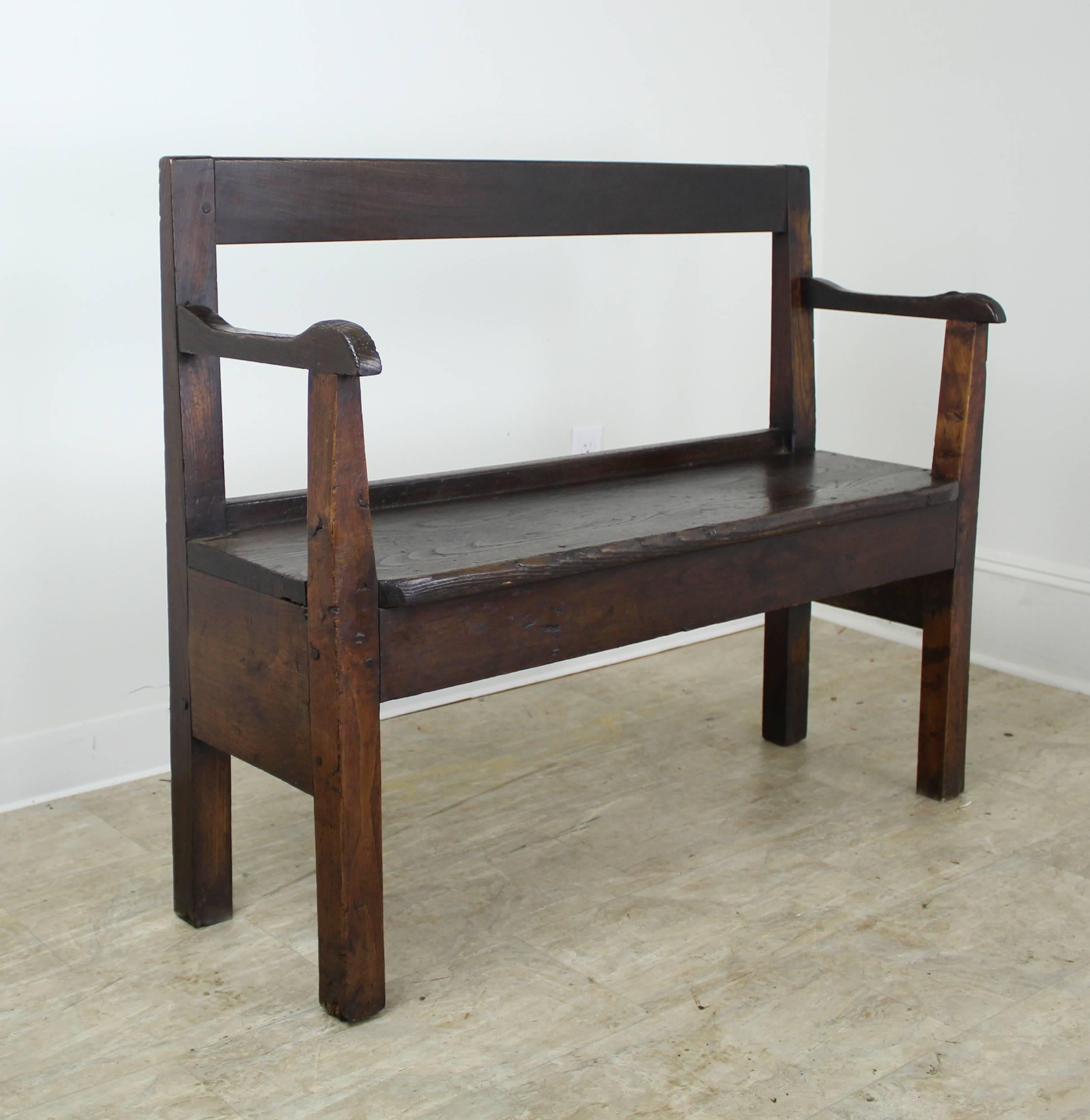 A very nice, rustic, sturdy bench, often found near the fireside. This piece has an open back and nice distress. Terrific deep color and patina. Well shaped arms offer a sweet design note.