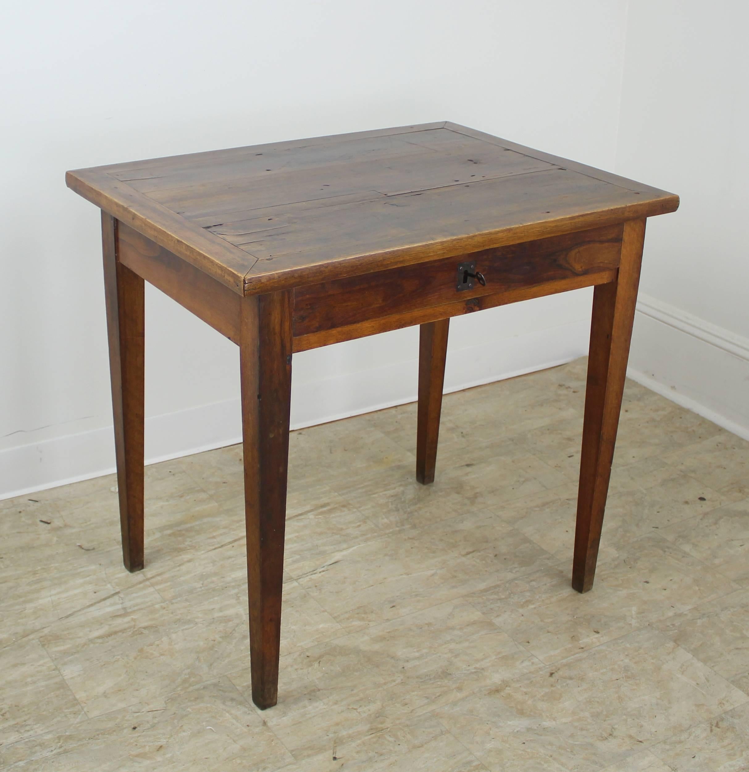 An elegant walnut side table with mitered corners on top, creating an interesting play of textures. Single drawer and long tapered legs. Beautiful patina and dramatic walnut grain. The large brass keyhole on the drawer has a working lock which adds