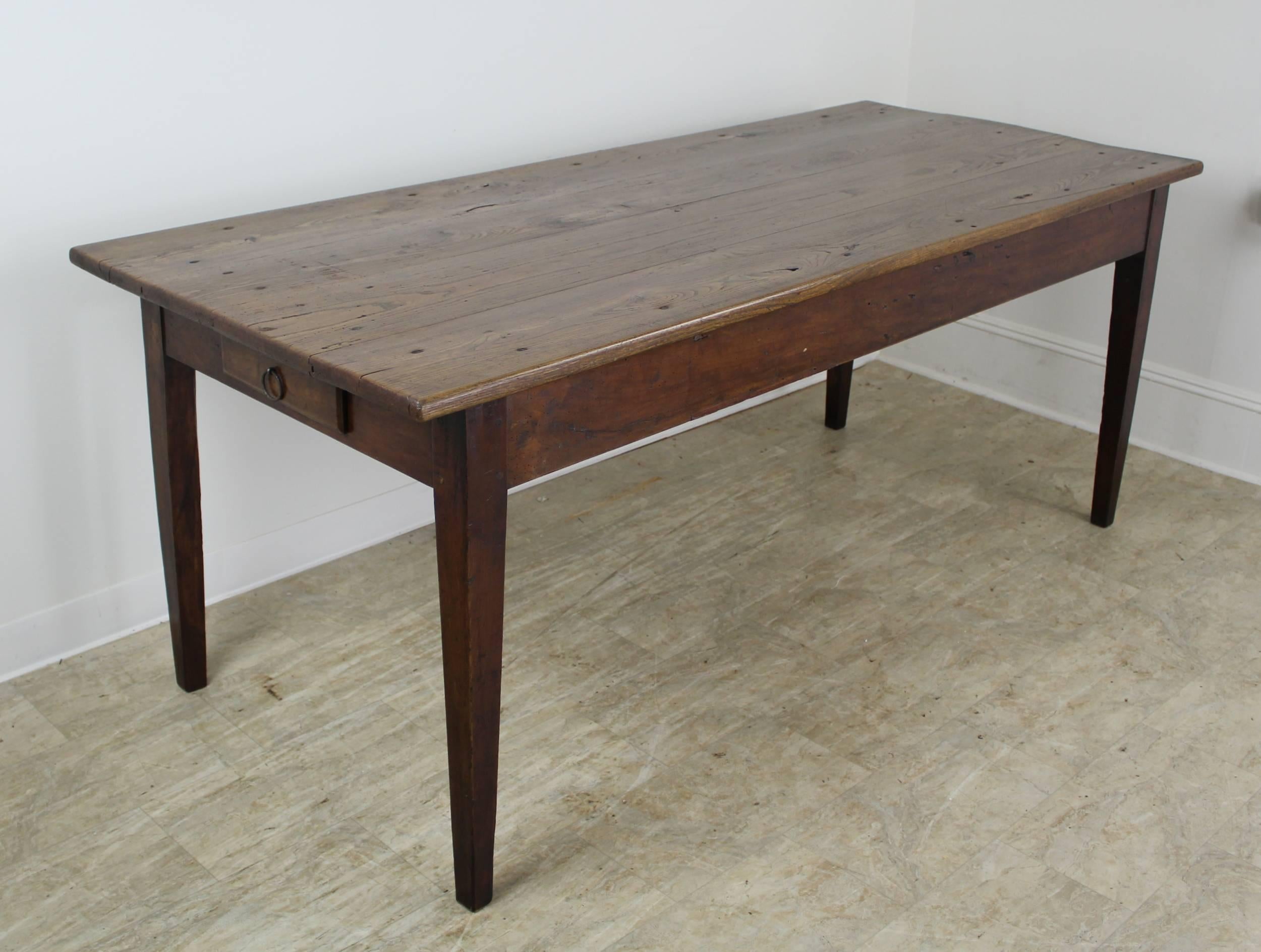 A handsome elm dining table or farm table with elegant tapered legs and a single drawer at the end. The top has lovely color, grain and patina. 24.5 inch apron height is good for knees and there are 68 inches between the legs on the long side.