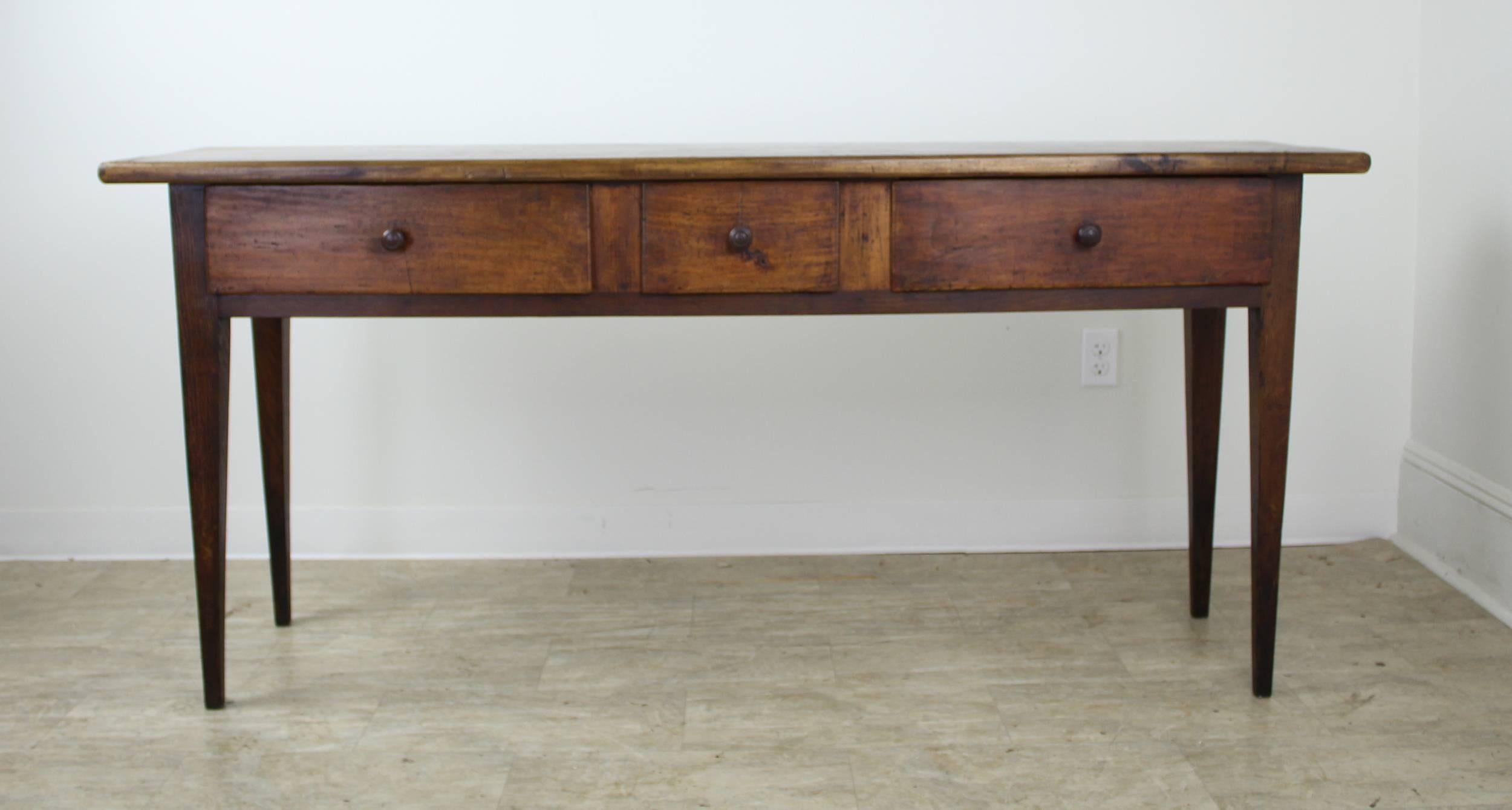 This richly colored poplar piece is a very impressive long console table with some interesting distress on top. Three drawers include a charming small center drawer. Legs are classic long and tapered country style, with sturdy pegs. Though longer,