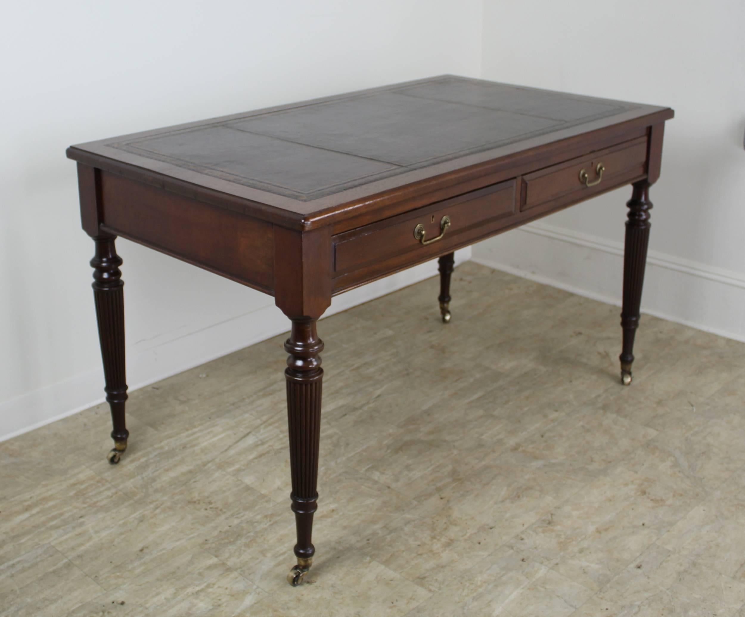 An elegant walnut desk in the Georgian style with eye-catching turned legs. Lovely brass castors and drop handles. Rich cordovan leather with gold embossed edges. Knee room a comfortable 24