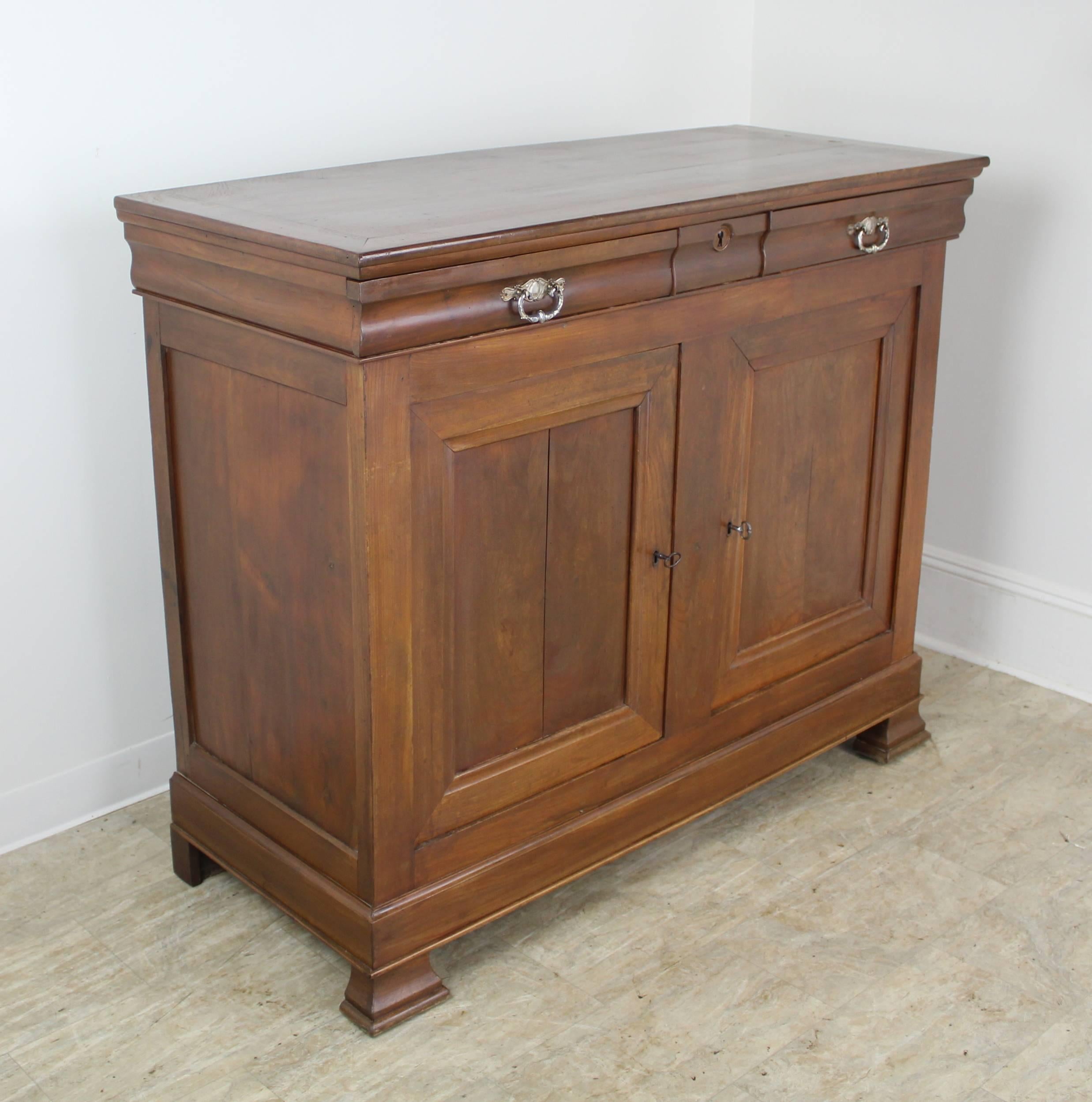 A Louis Philippe buffet with an additional decorative touch--this sideboard has very pretty distressed silver plate handles. Mitred corners at the top, and two drawers over two doors offer good storage space. The walnut grain is lovely, and the