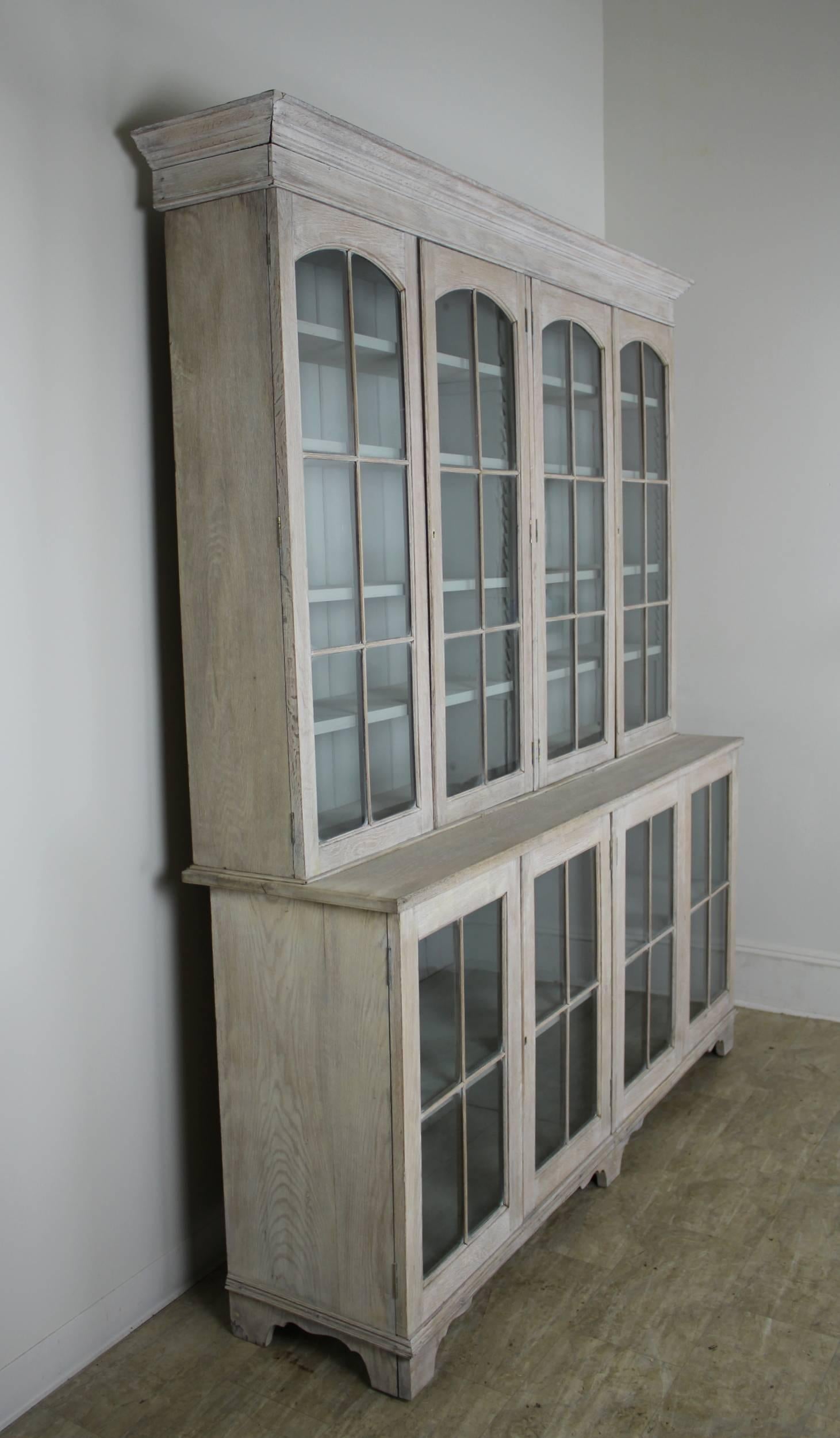 An elegant early English oak bookcase, bleached for a clean and modern look. Top and bottom components come apart for easy transport., with adjustable shelving top and bottom. The interior of this piece has been newly painted a serene light