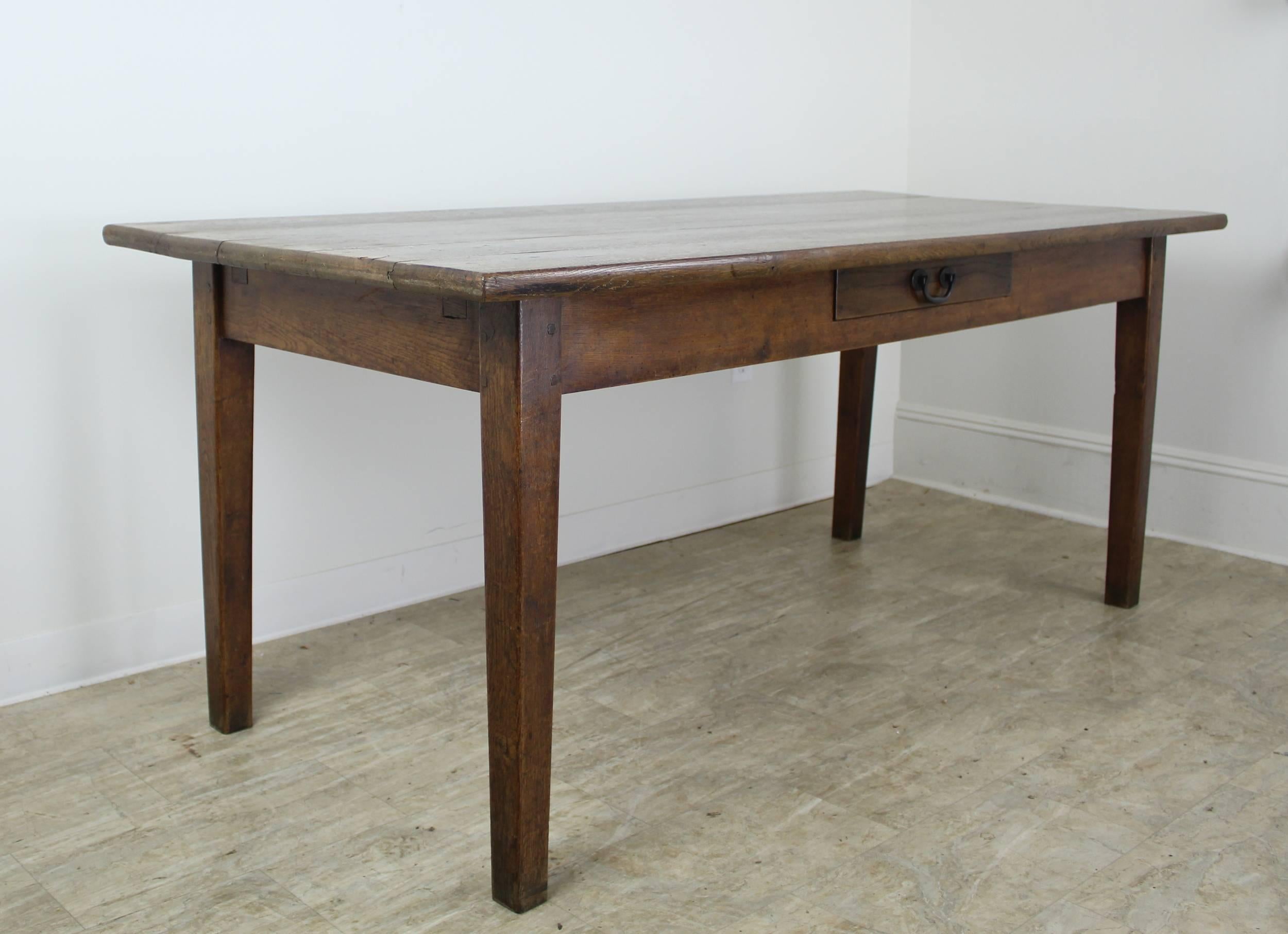 A sturdy and handsome French oak farm table with classic tapered legs, a thick top and single drawer for visual interest. The color and grain on this table are lovely, as is the patina and shine. The 24 inch apron height is good for knees. 60 inches