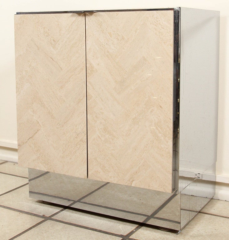 Beautiful pair of cabinets by Ello. They are veneered in polished travertine laid in a chevron pattern. The door handles, trim and cabinet sides are chromed. One cabinet has an open interior, the other has shelves.