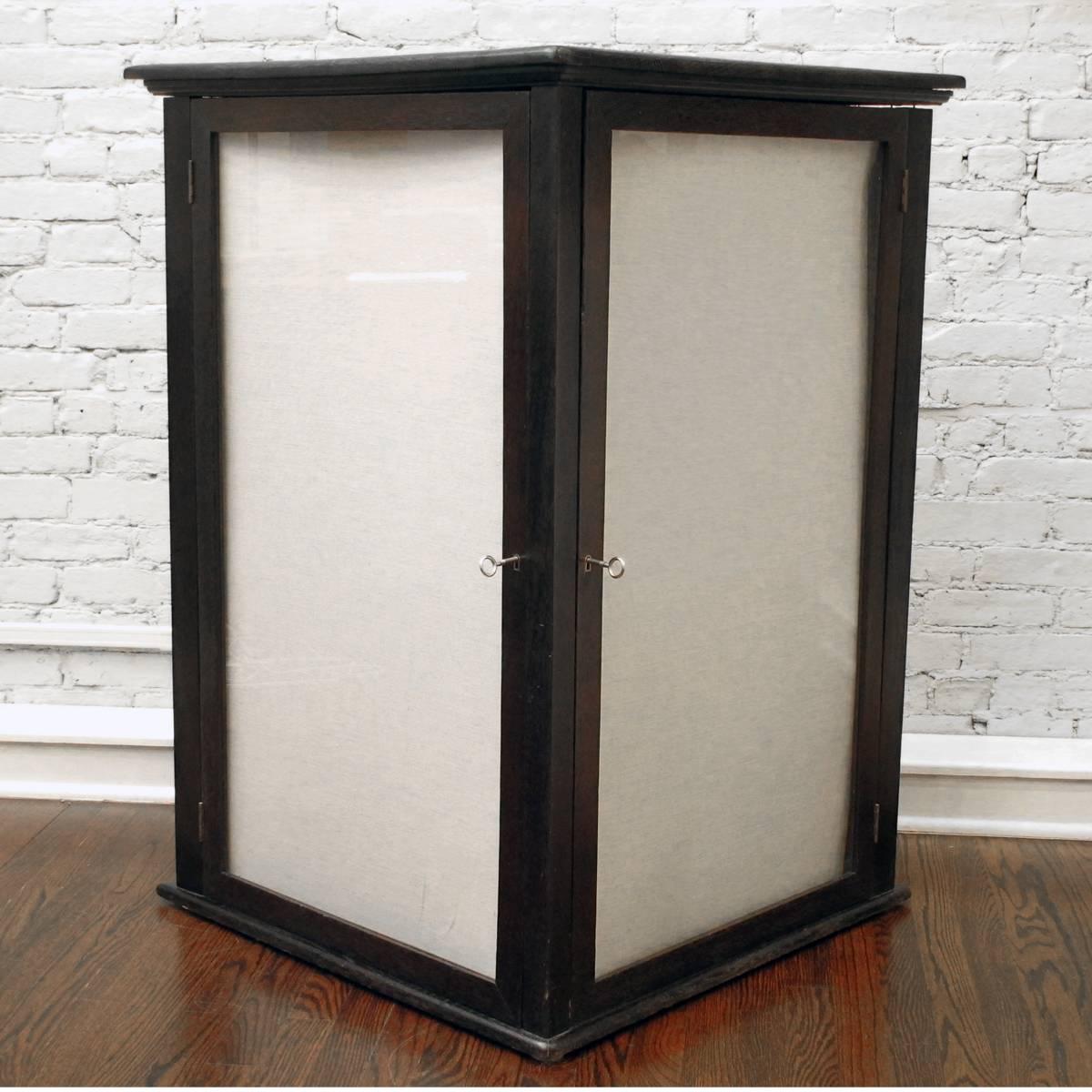 Triangular oak store display case, comprised of two shallow display cabinets with glass doors, and a storage cabinet with three fixed shelves behind a paneled door. Refinished, and with new nickel skeleton keys/locks. Originally for displaying