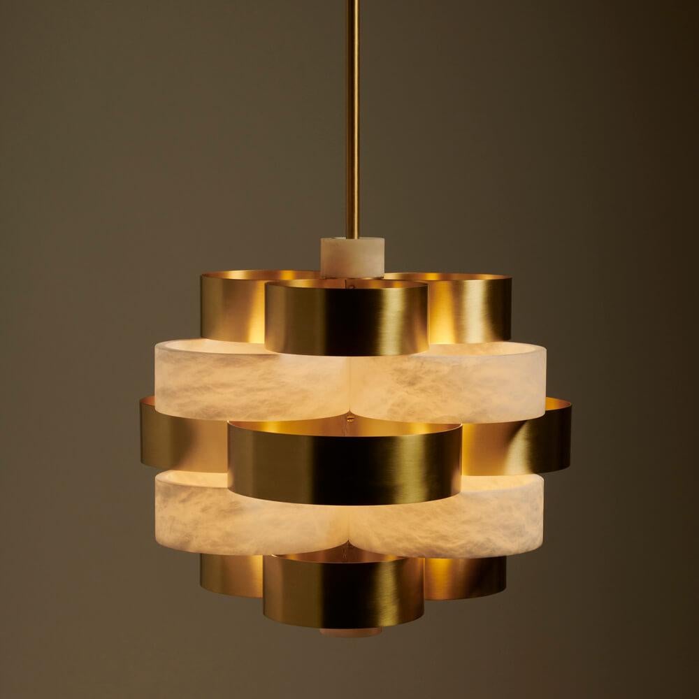 Vertigo is an eye-catching pendant chandelier with a sculptural presence, composed of alternating rings of satin brass and natural alabaster. Its spherical structure, both harmonious and elegant, sculpts light into a warm and enveloping glow, making