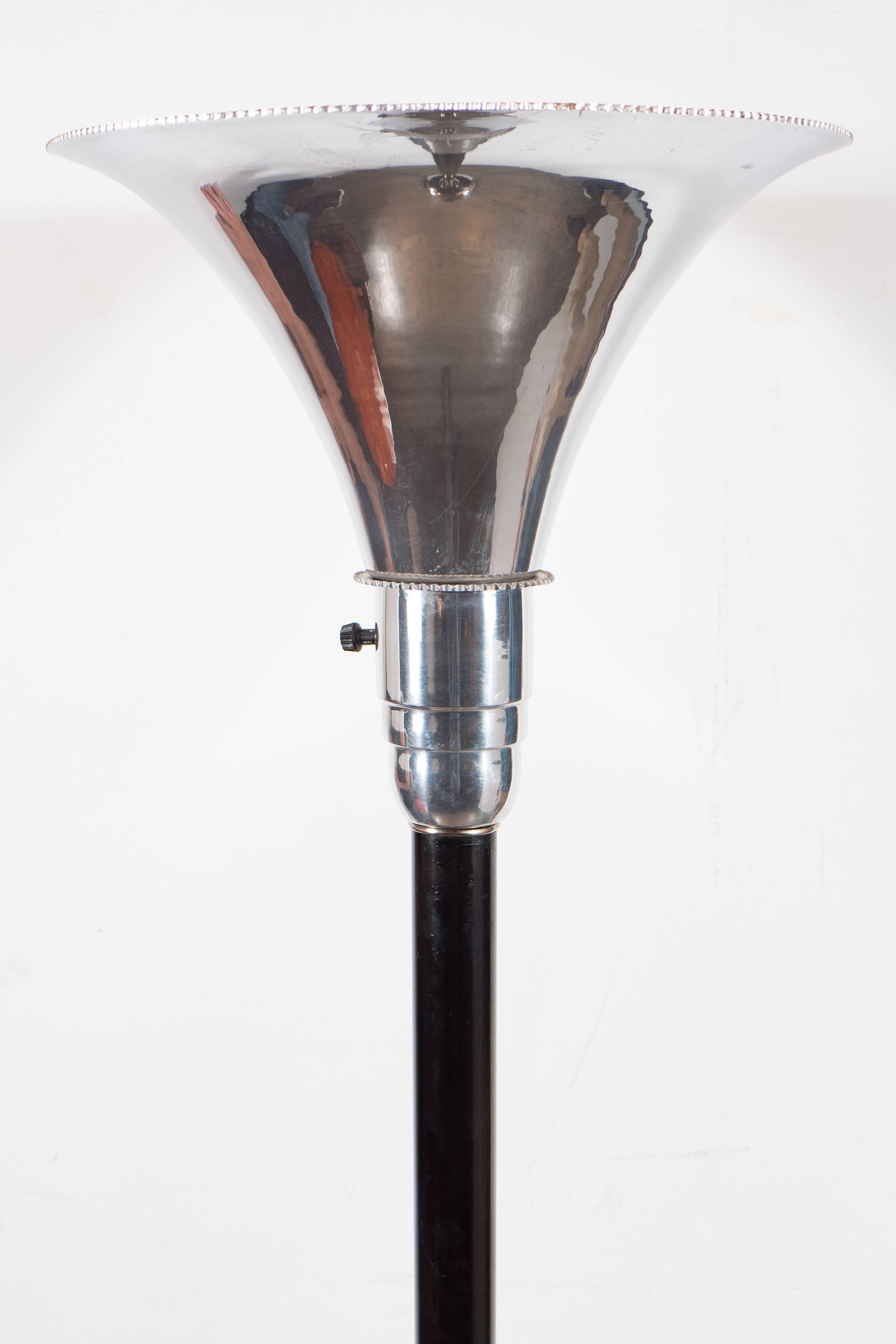 An Art Deco Machine Age torchiere. The base is a concentric circular design in contrasting black enamel and polished aluminum, the stem is also finished in black enamel, it supports a polished aluminum funnel shaped shade with a serrated detail