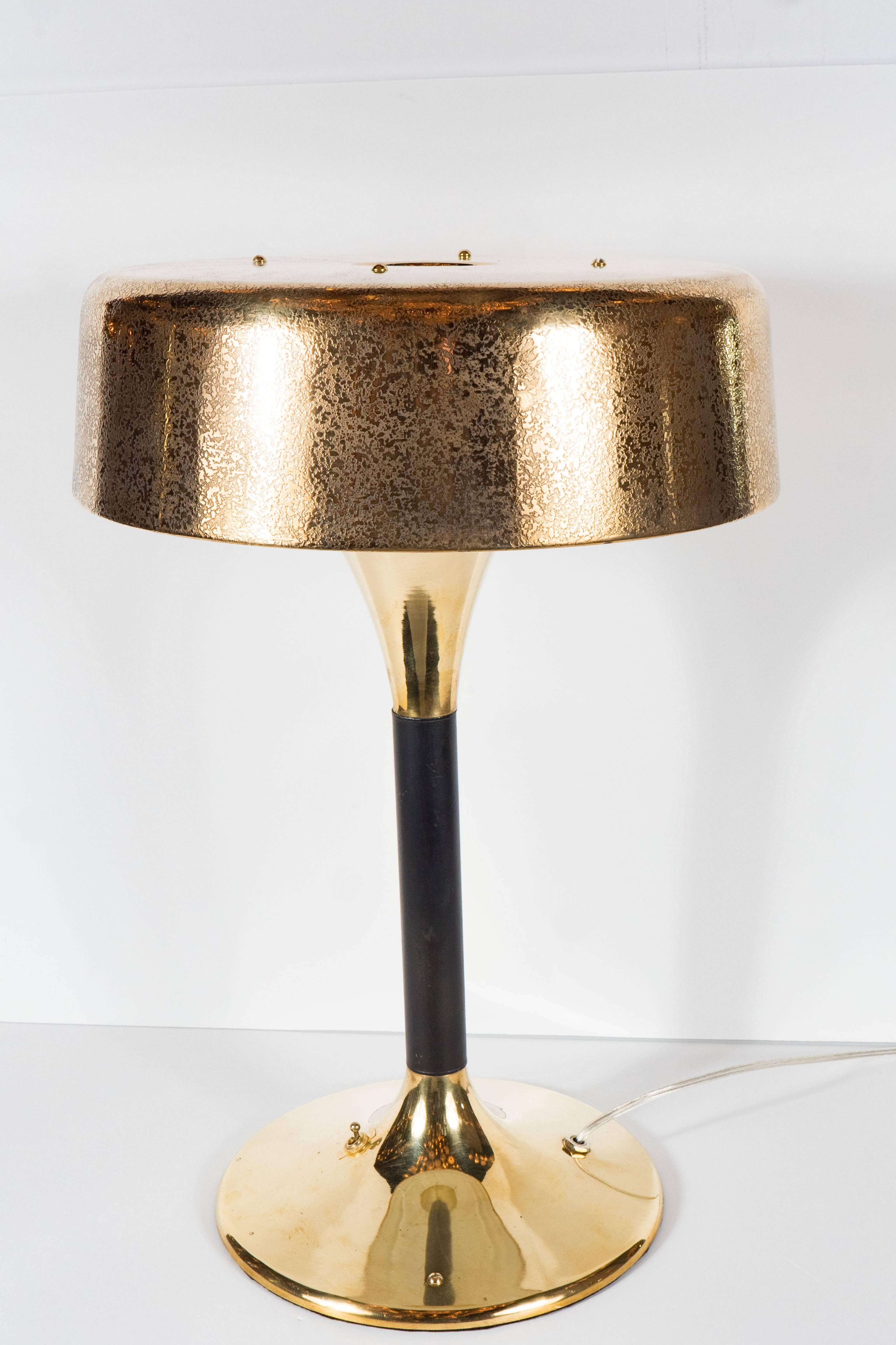This stunning lamp from an Italian cruise ship features a splayed circular conical base in polished brass that still retains the original switch that reads on and off. It has a black enamel stem and it is fitted with a flared cap that reaches up to