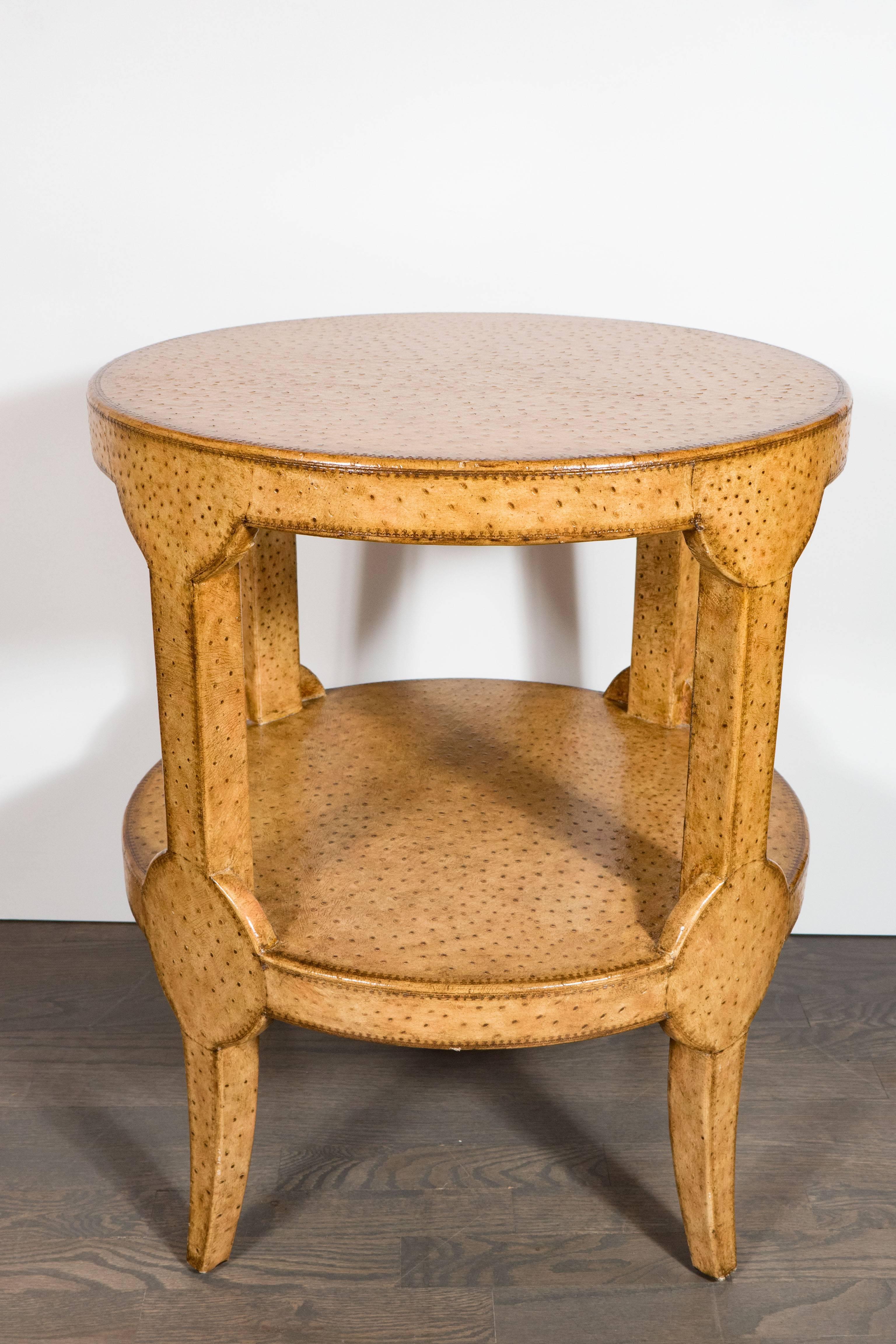 A Mid-Century Modernist two-tier ostrich leather gueridon side table. Fully covered in soft butterscotch-colored ostrich, slightly splayed legs support two circular tiers. Stitching along perimeter of the piece. Excellent craftsmanship and high