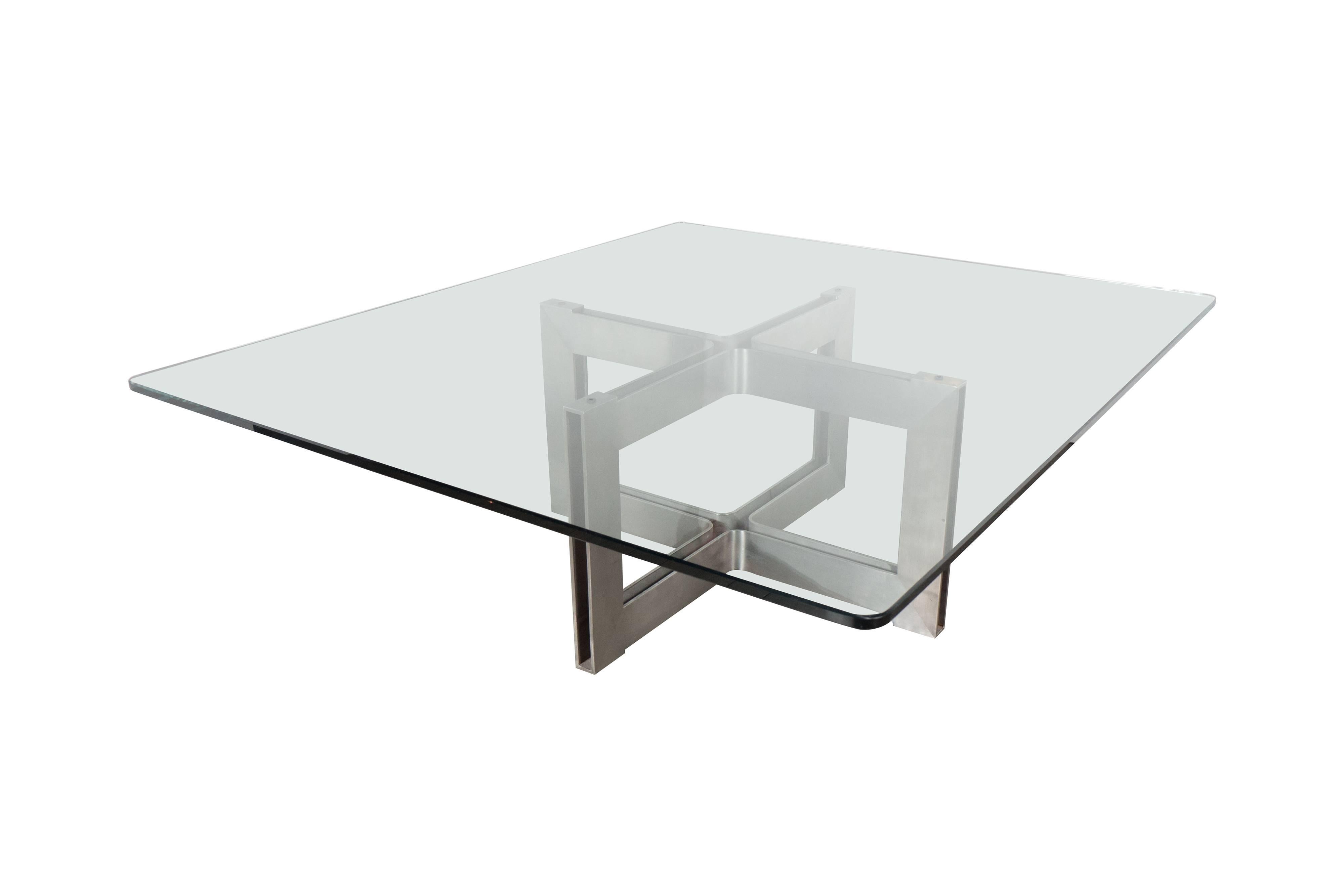 A Mid-Century Modernist steel X-base cocktail table in the manner of Roger Sprunger. A brushed steel frame supports a soft polished, rounded edge 1/2 inch clear glass top. The brushed steal lends to an Industrial style while the design is clearly