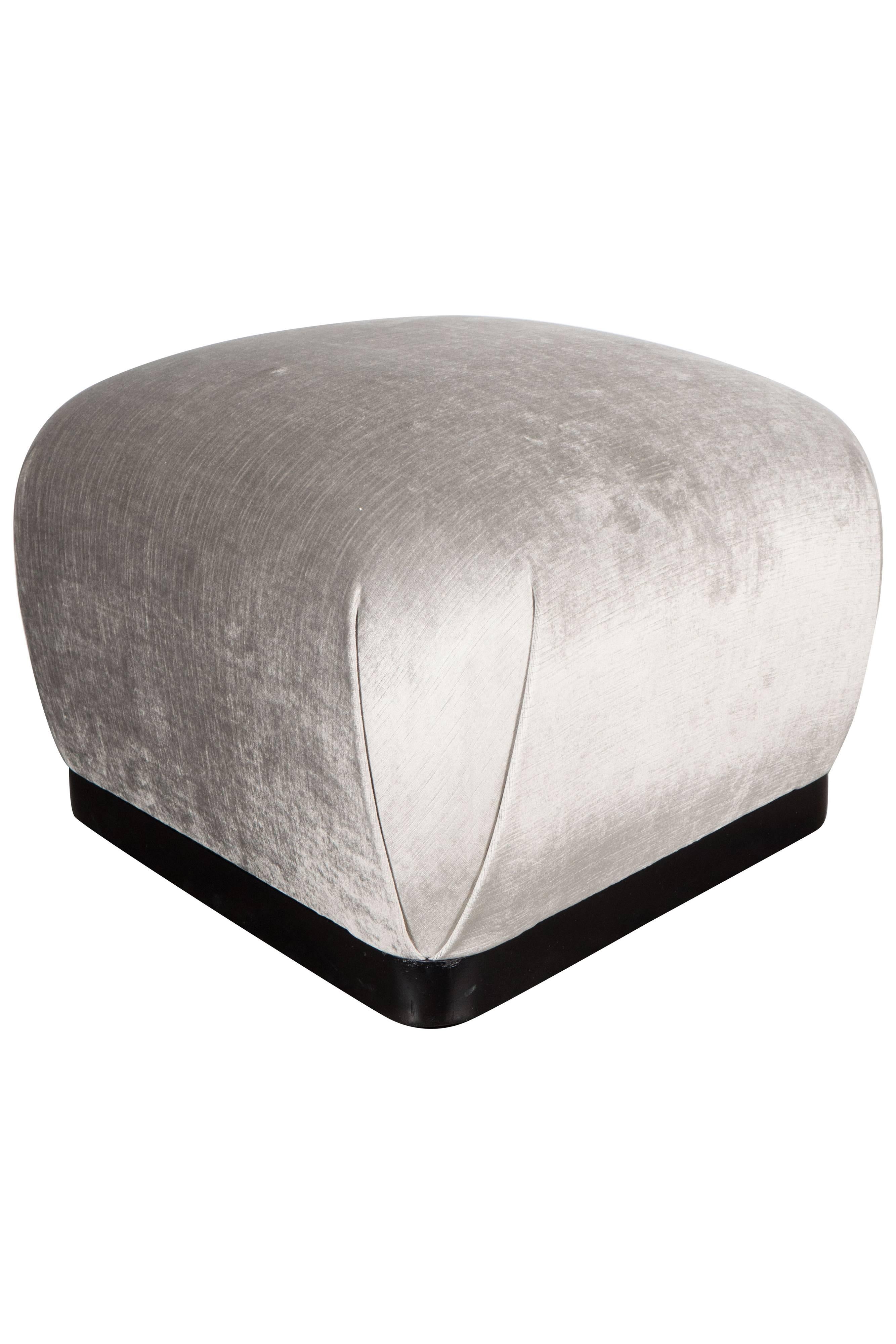 A Souffle style ottoman in smoked platinum velvet in the manner of Karl Springer. An ebonized walnut base with gliders supports a rounded cushion, newly upholstered in a luxe smoked platinum velvet fabric. It can be used as an ottoman, additional