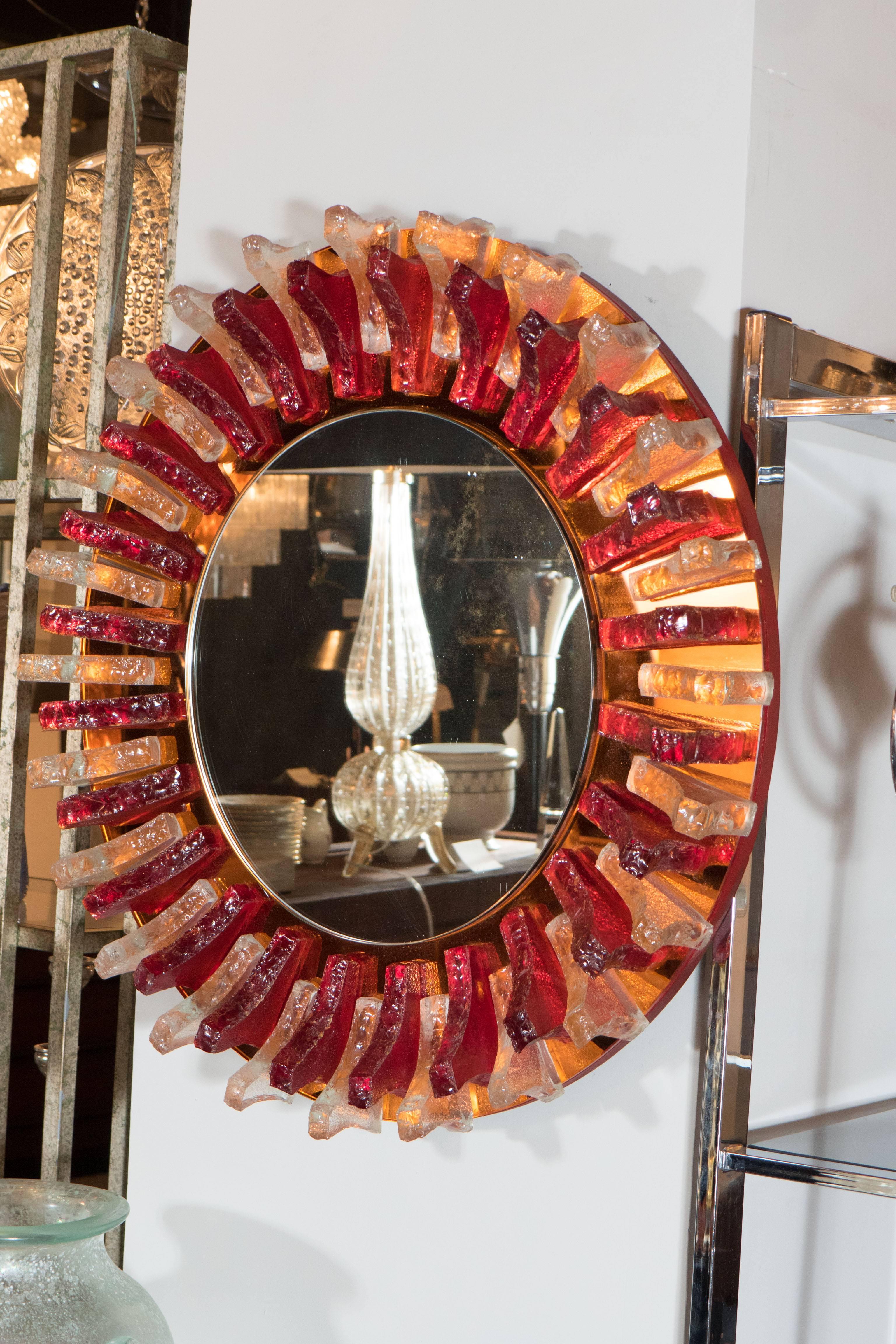 A stunning Mid-Century Modernist circular mirror with alternating garnet and clear fin-like resin appliques on an amber mirror border. A striking piece for an entry or foyer. It is in excellent condition.