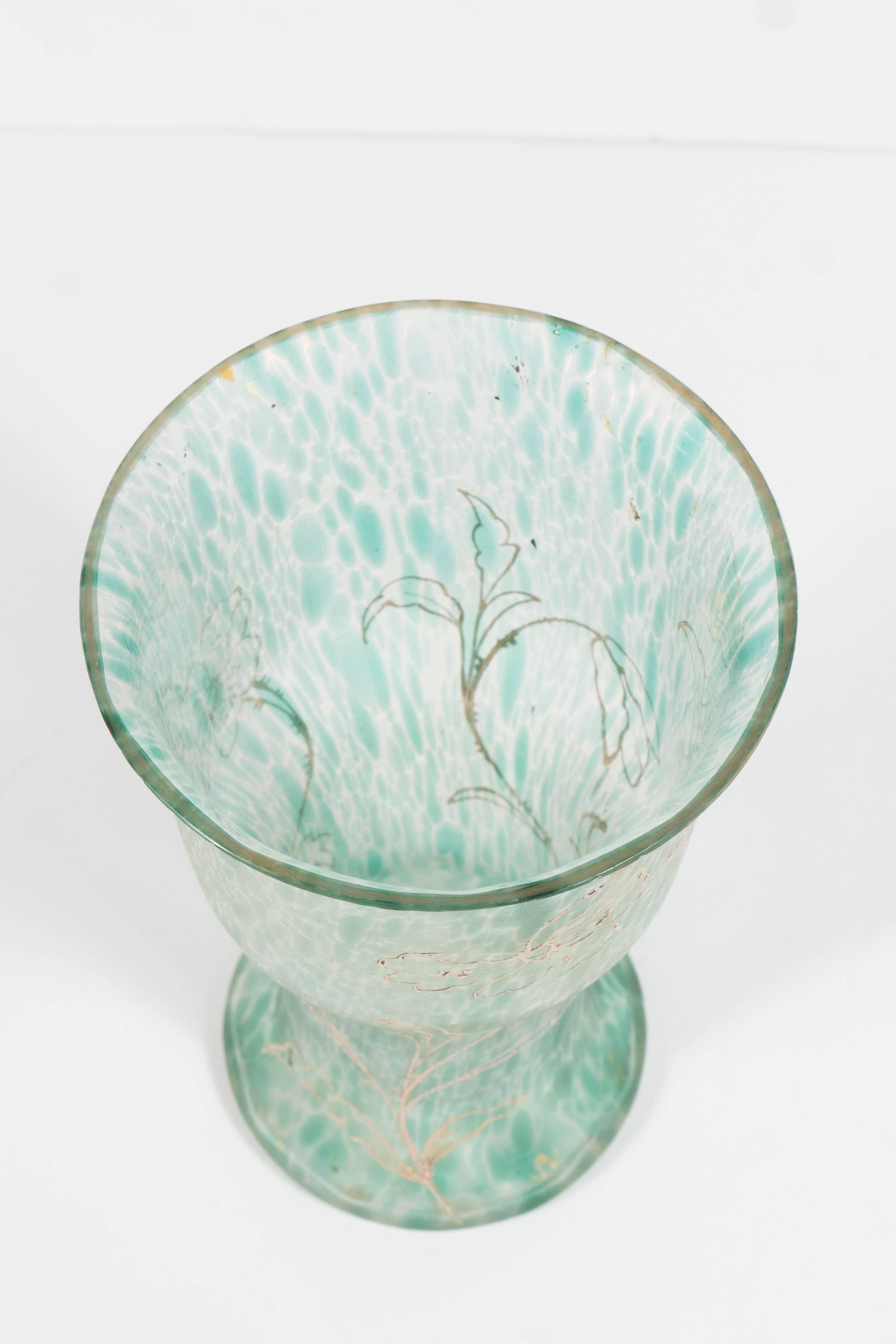 This gorgeous Art Nouveau handblown glass vase features a mottled pattern throughout, consisting of a constellation of celadon flecks suspended in translucent glass. A scrolling foliate pattern resembling a blooming poppy plant is inscribed on the