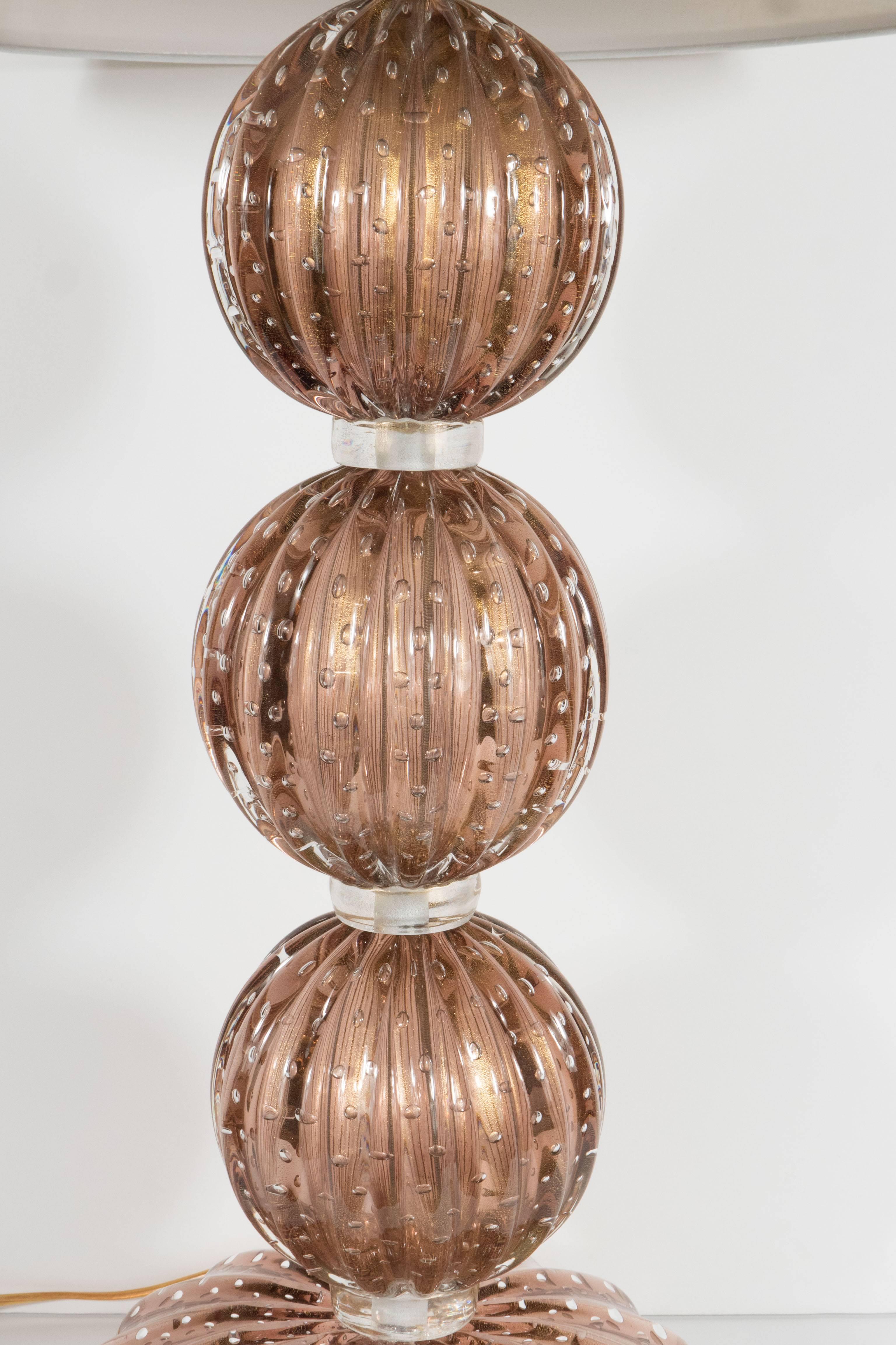 This exquisite pair of Mid-Century Modernist Murano glass table lamps feature a stacked sphere design in a smoked amethyst color separated by a clear band. The glass features a fluted detail with 24-karat gold flecks and controlled release bubbles