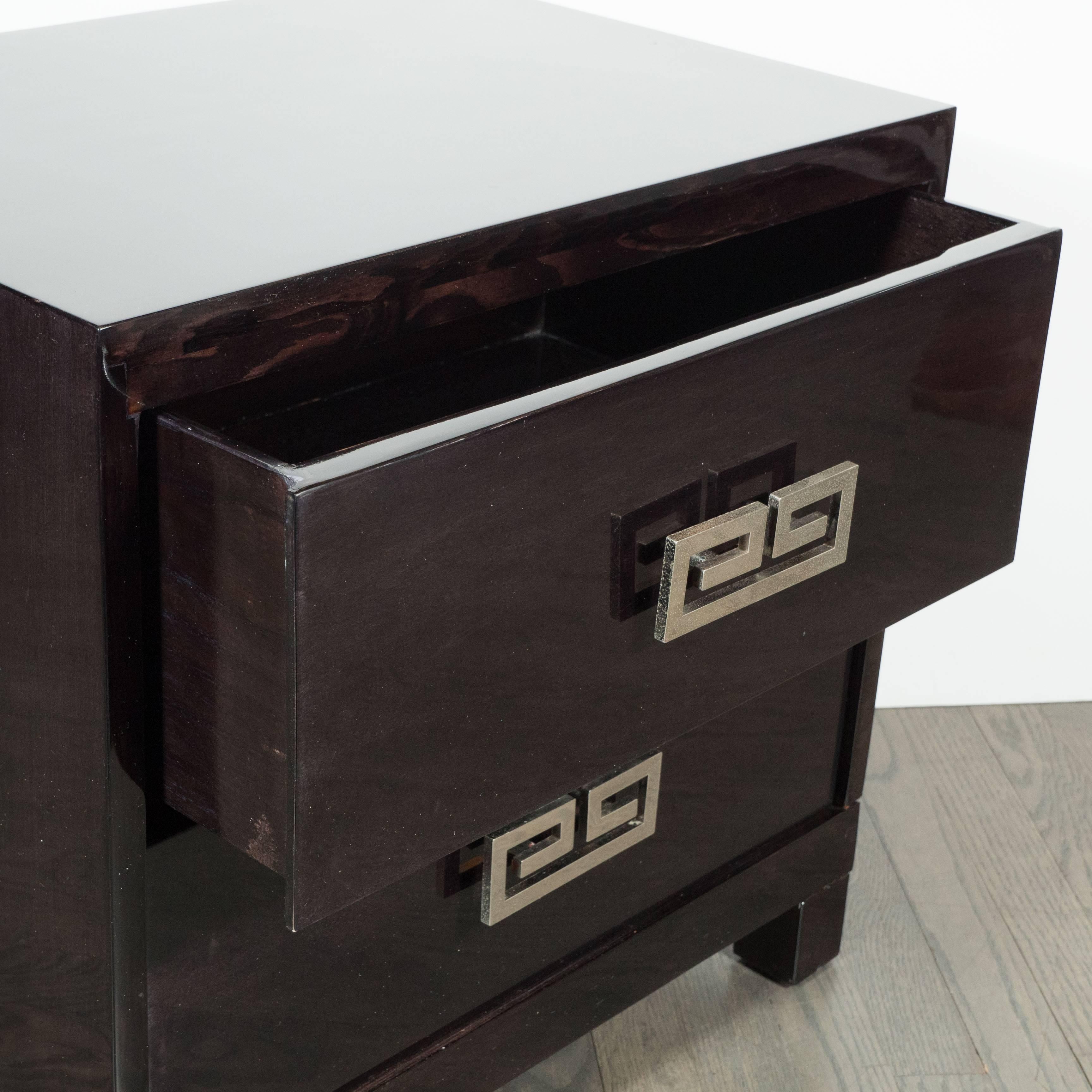 This stunning pair of Mid-Century end tables or nightstands were realized in the United States, circa 1950. They feature rectilinear bodies and volumetric square feet in hand-rubbed ebonized walnut fitted with two drawers each. They offer polished