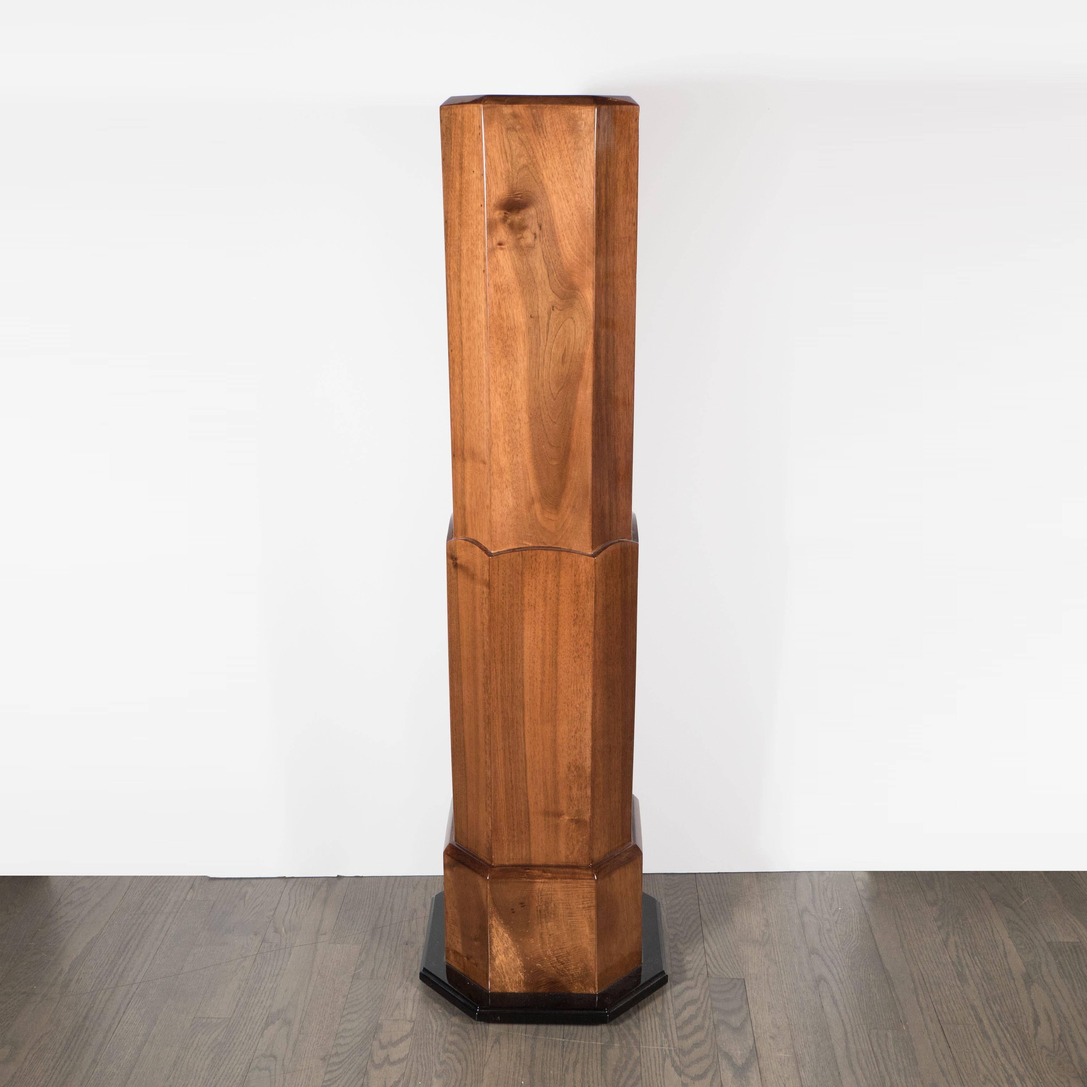 An Art Deco skyscraper-style pedestal in bookmatched walnut with black lacquer accents. A stepped design gives this octagonal pedestal a statuesque disposition. A ebonized and lacquered base supports the piece, with beveled and scalloped detailing